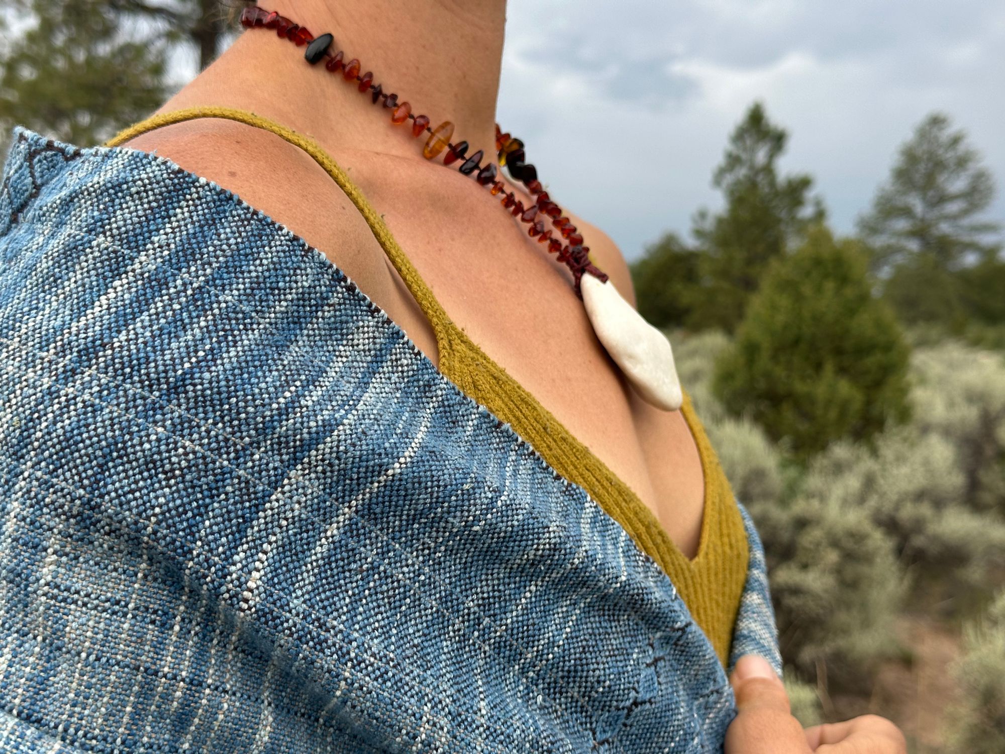 a 4.6 meter piece of handwoven fabric that is indigo blue and deep walnut dyed brown wrapped around the shoulders of a woman wearing an amber necklace