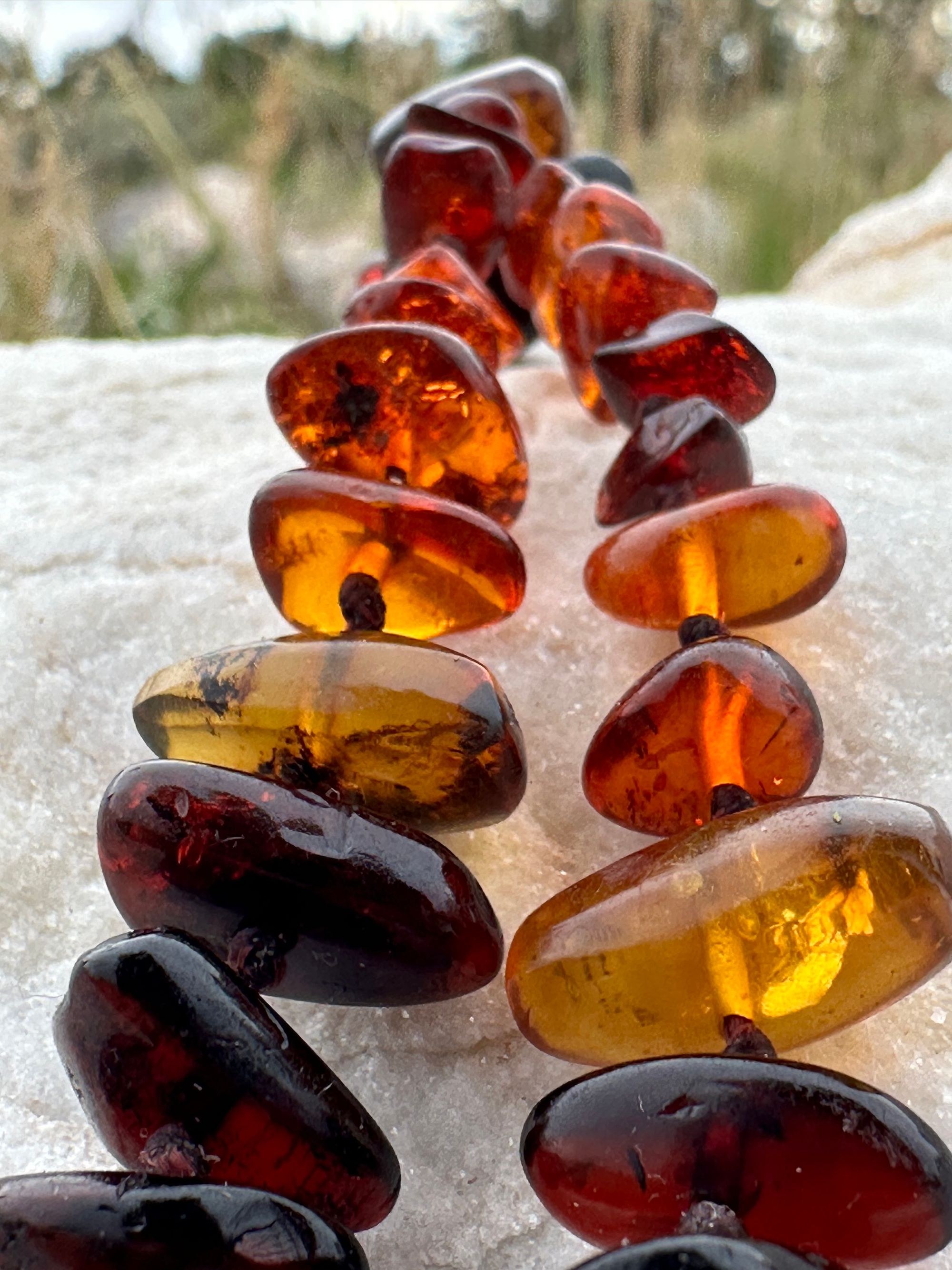 A detail of A necklace made of white river tumbled marble in a soft diamond shape is joined by beads of deep red orange Amber