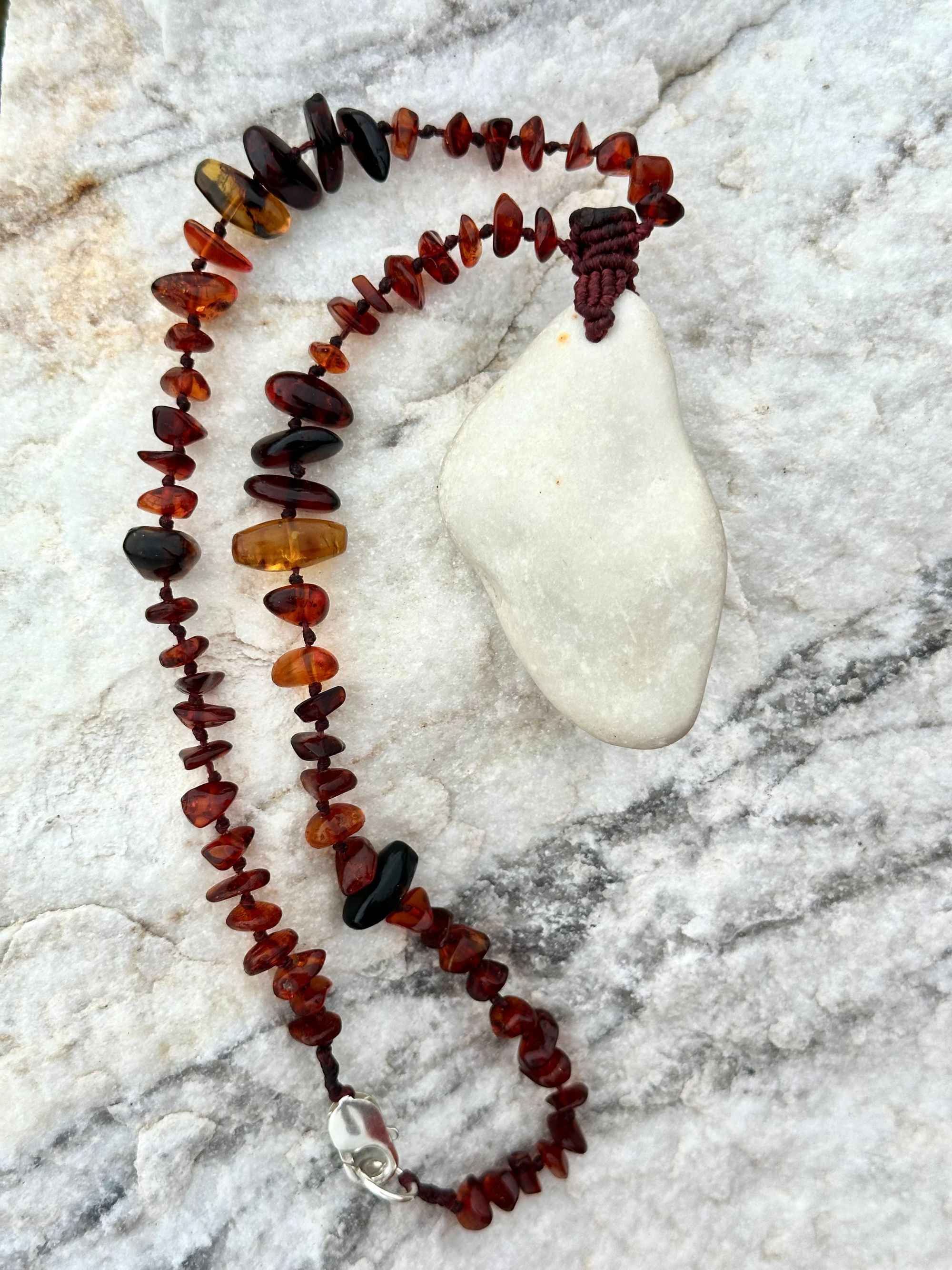 A necklace made of white river tumbled marble in a soft diamond shape is joined by beads of deep red orange Amber