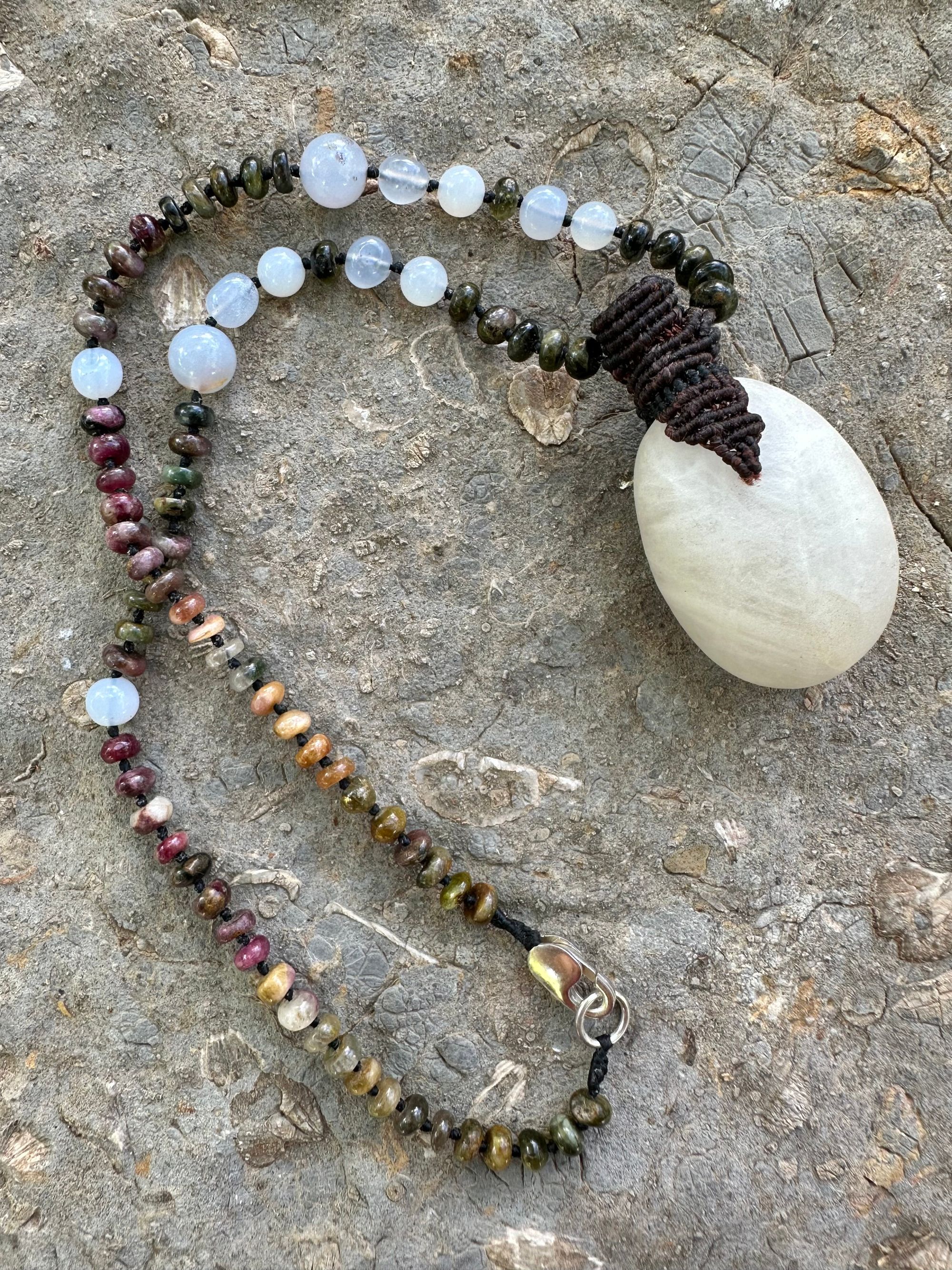 A necklace of an oval white ocean tumbled stone with a knot work vessel Growing from it is held by beads of luminous blue chalcedony and orange green, yellow and pink tourmaline