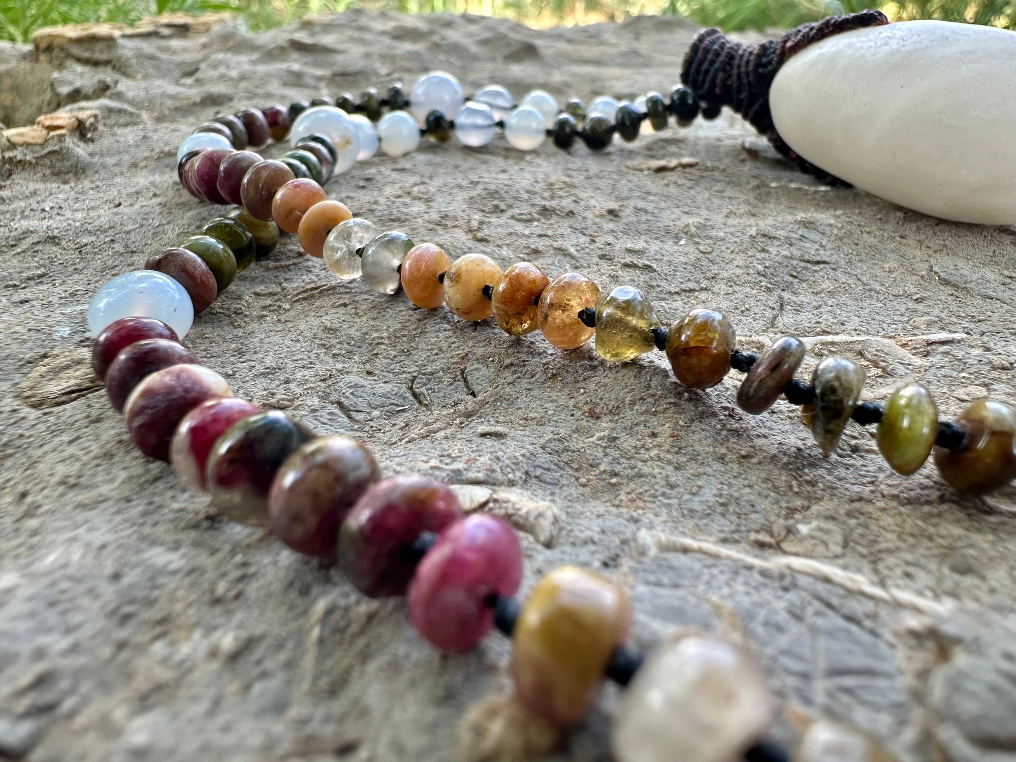 A necklace of an oval white ocean tumbled stone with a knot work vessel Growing from it is held by beads of luminous blue chalcedony and orange green, yellow and pink tourmaline