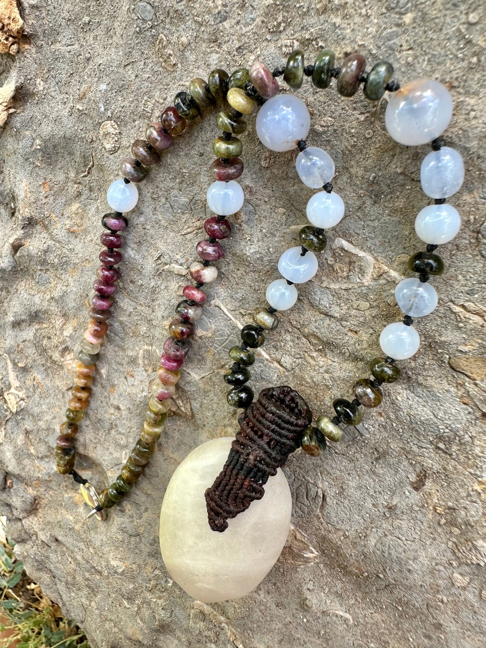 A necklace of an oval white ocean tumbled stone with a knot work vessel Growing from it is held by beads of luminous blue chalcedony and orange green, yellow and pink tourmaline