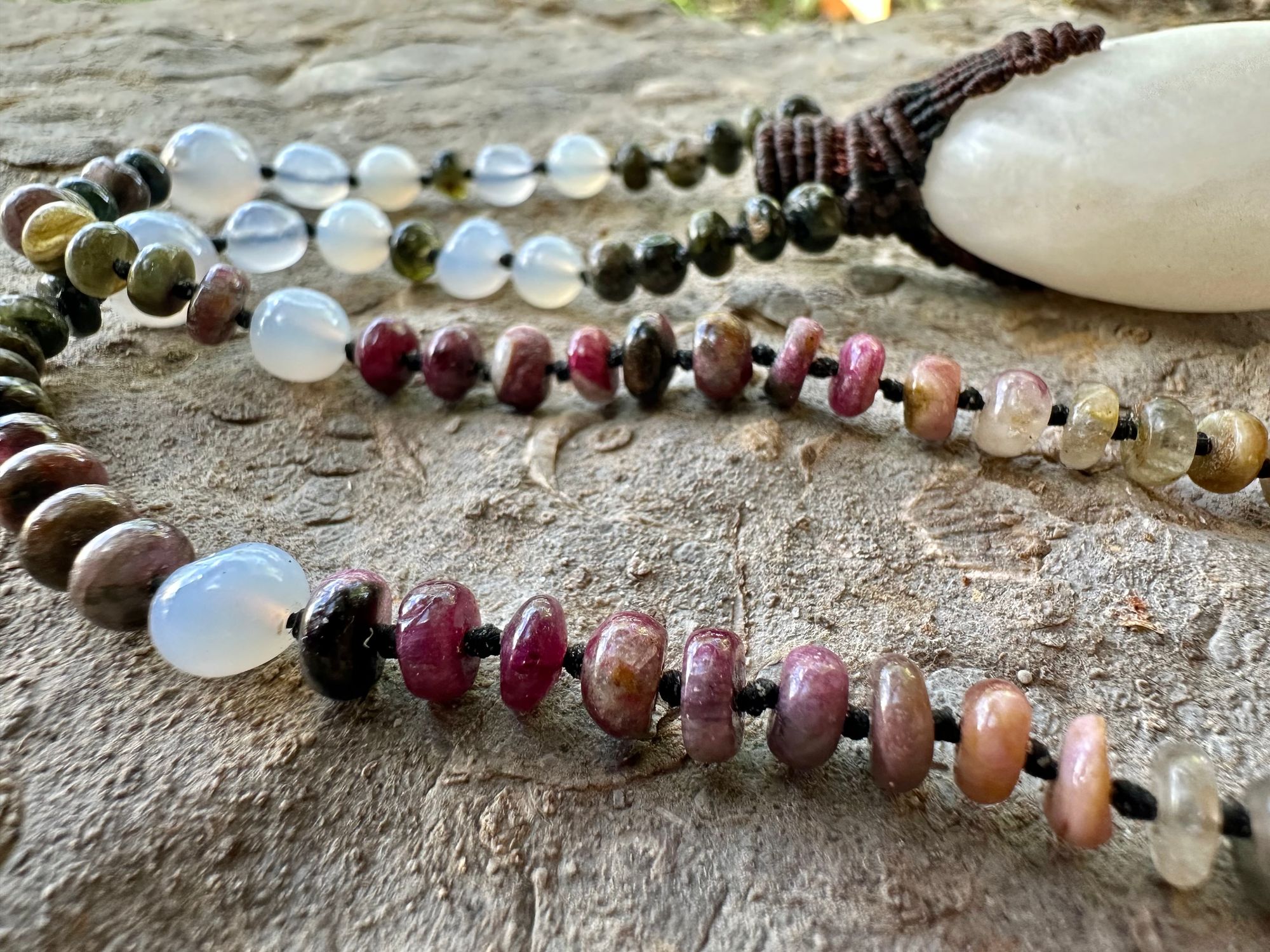 A necklace of an oval white ocean tumbled stone with a knot work vessel Growing from it is held by beads of luminous blue chalcedony and orange green, yellow and pink tourmaline