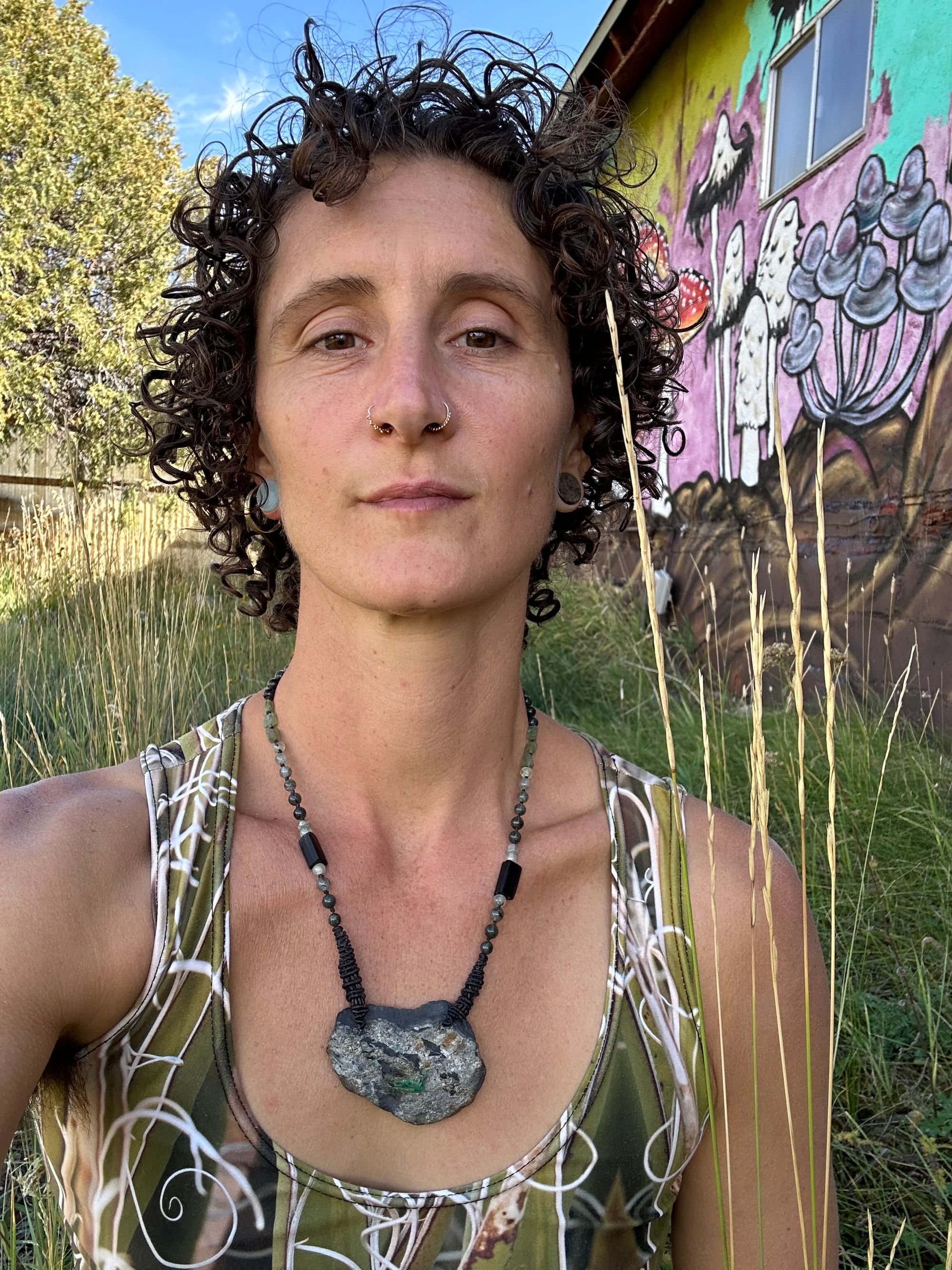 A woman wears In necklace of raw emerald in its matrix with glittering pyrite is hanging from strands of delicate black work with green beads of rutile, quartz, peridot and black tourmaline