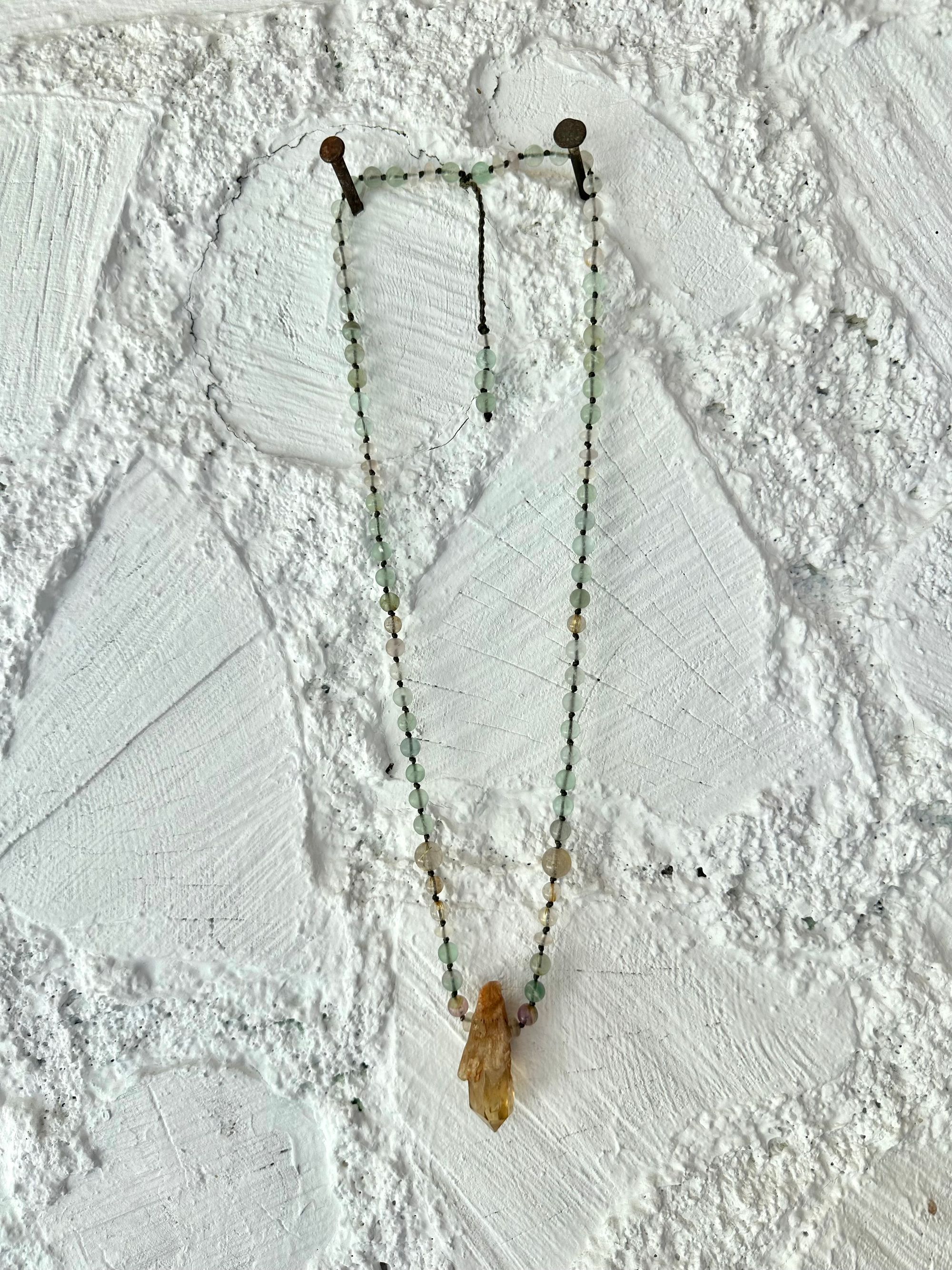  A necklace of Yellow citrine, Purple and green fluorite and brilliant golden rutile quartz Hang on a white painted cordwood wall