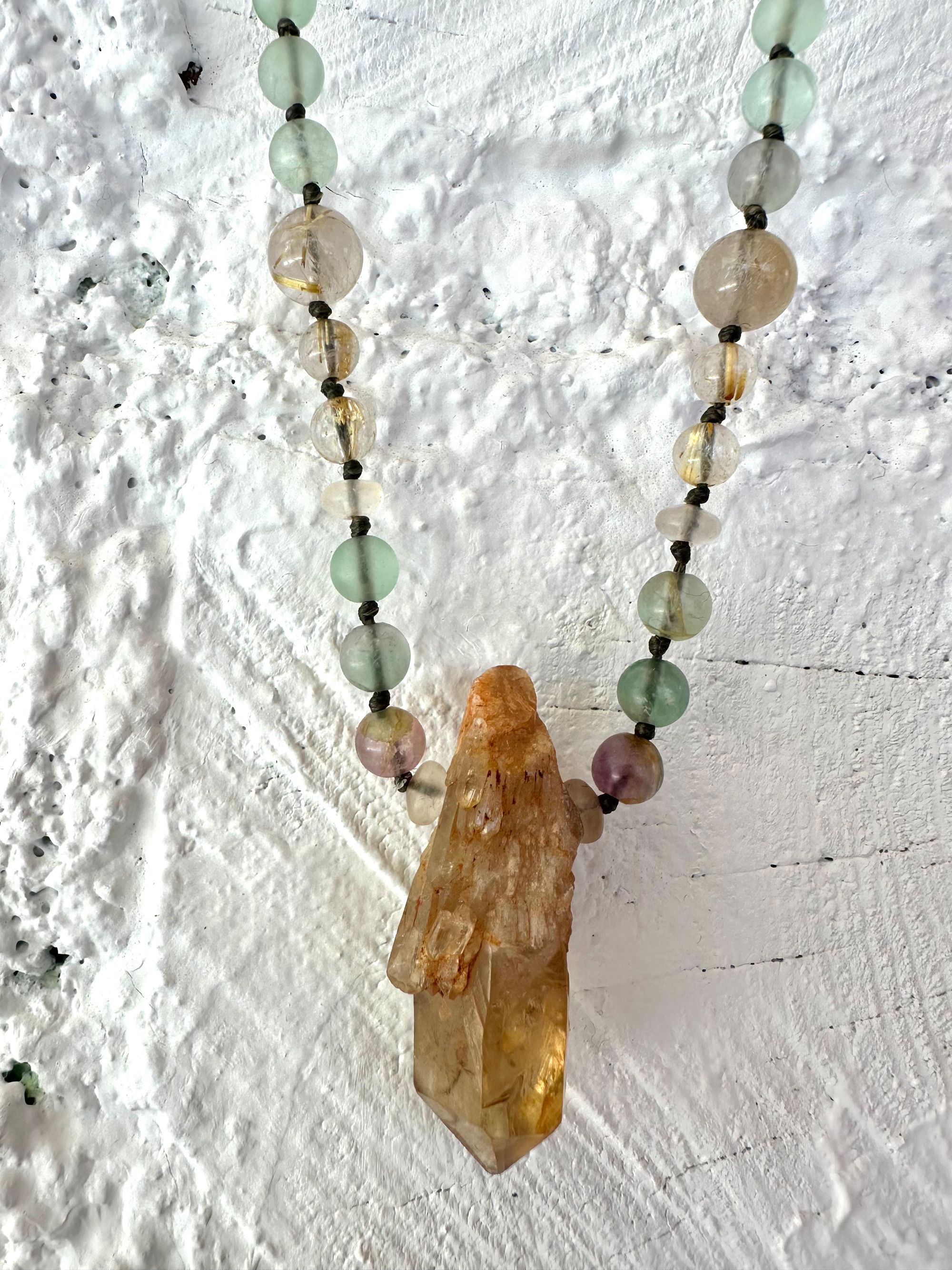  A necklace of Yellow citrine, Purple and green fluorite and brilliant golden rutile quartz Hang on a white painted cordwood wall