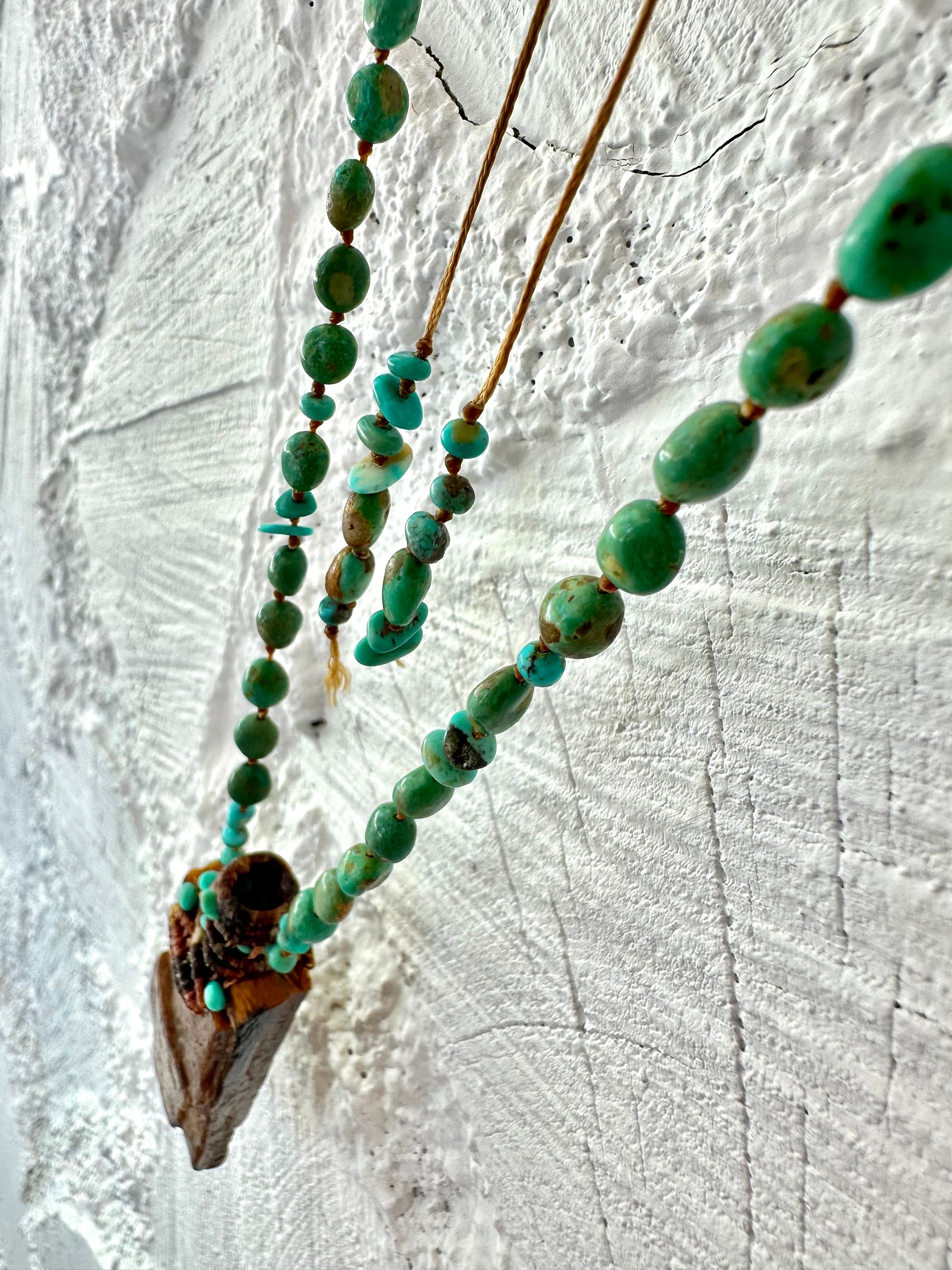 A necklace made of petrified wood, tiny net work basket and turquoise hangs against a white painted cordwood wall