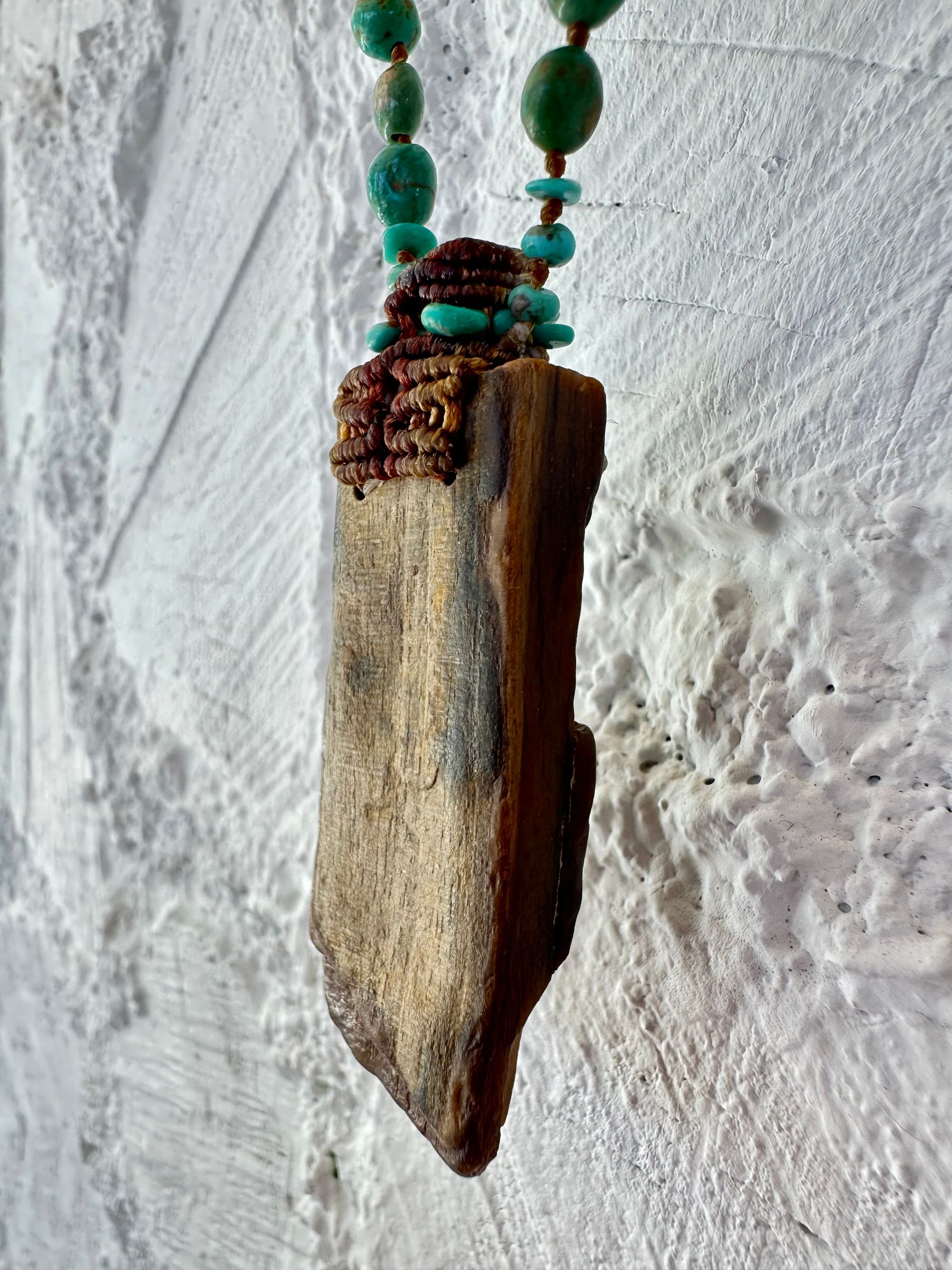 A necklace made of petrified wood, tiny net work basket and turquoise hangs against a white painted cordwood wall