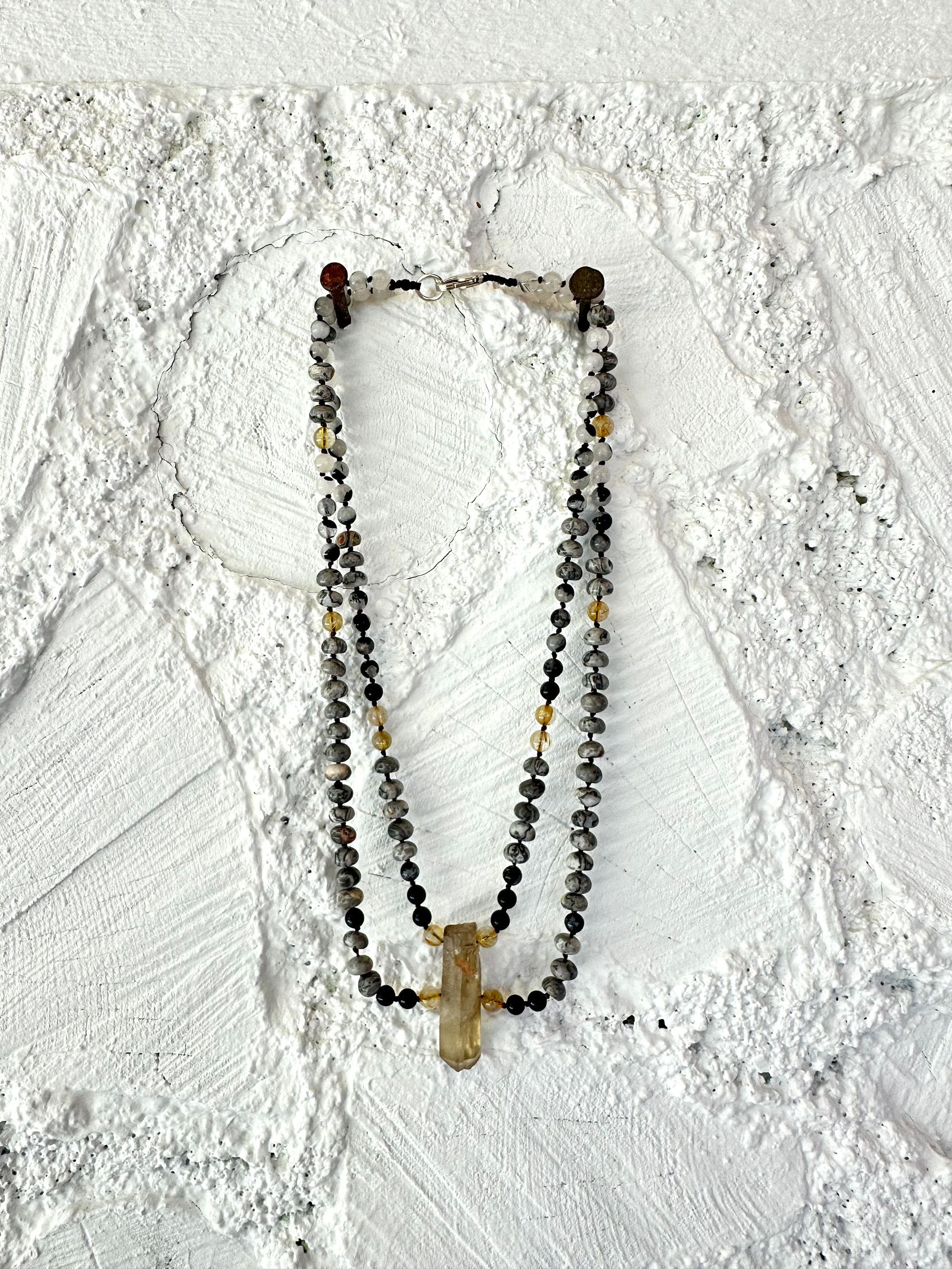 Golden yellow citrine hangs from two strands of gold, rutile, quartz, black, rutile, quartz, and Lacey Gray picture Jasper against a wall of white painted Cordwood