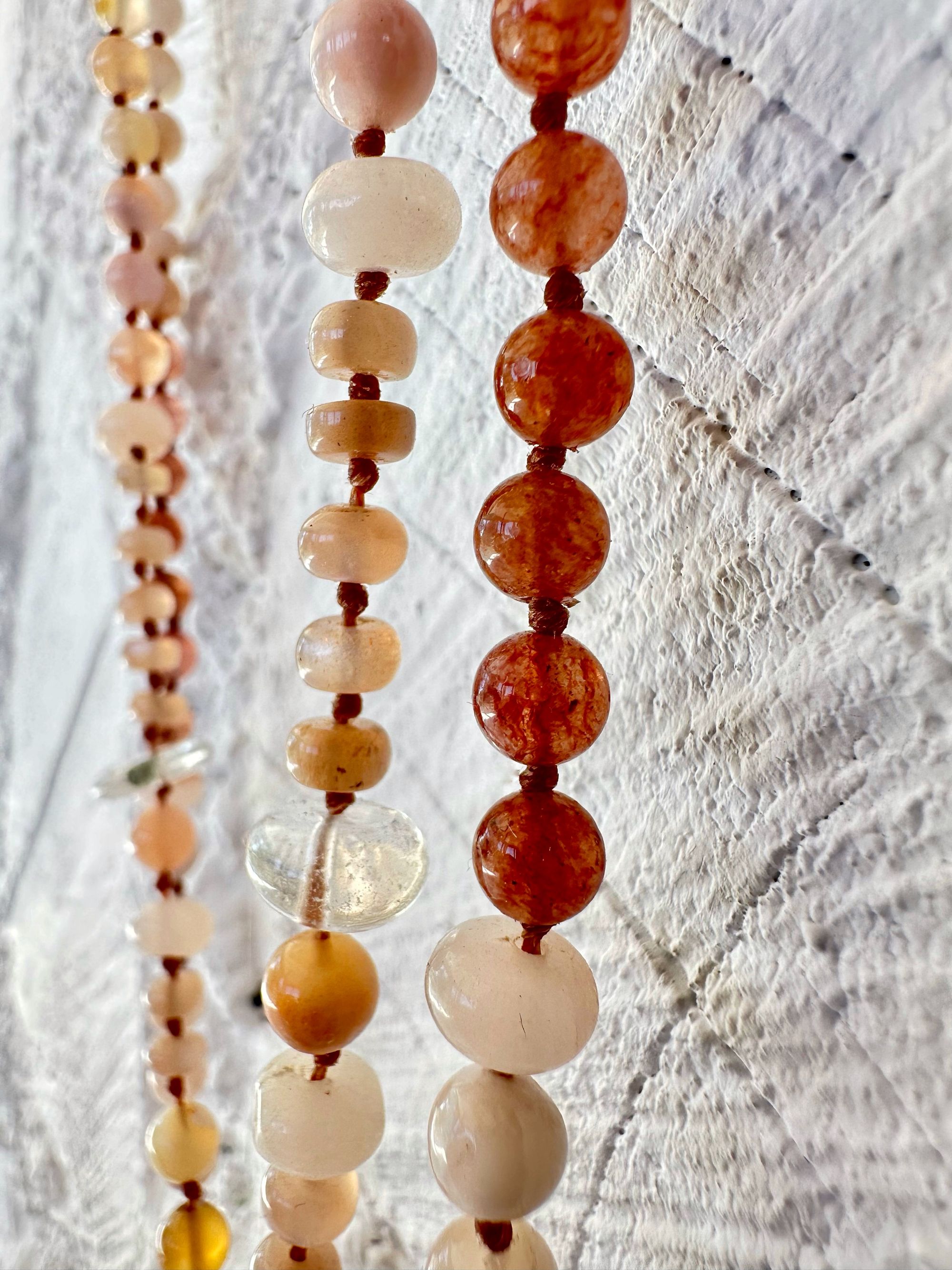 A necklace of clear, vibrant pink And luscious rose, semi precious stones has two strands and hangs against a white painted cordwood wall