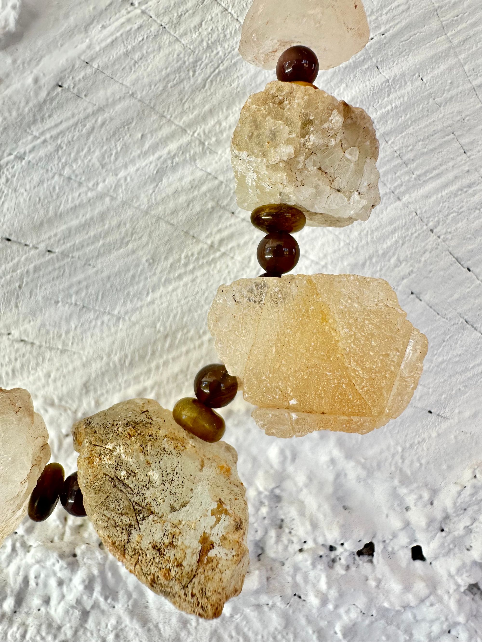 10 light green nuggets of fluorite are joined by dark, gray and brown beads of egg and tiger eye in a necklace, hanging on a white painted cordwood wall