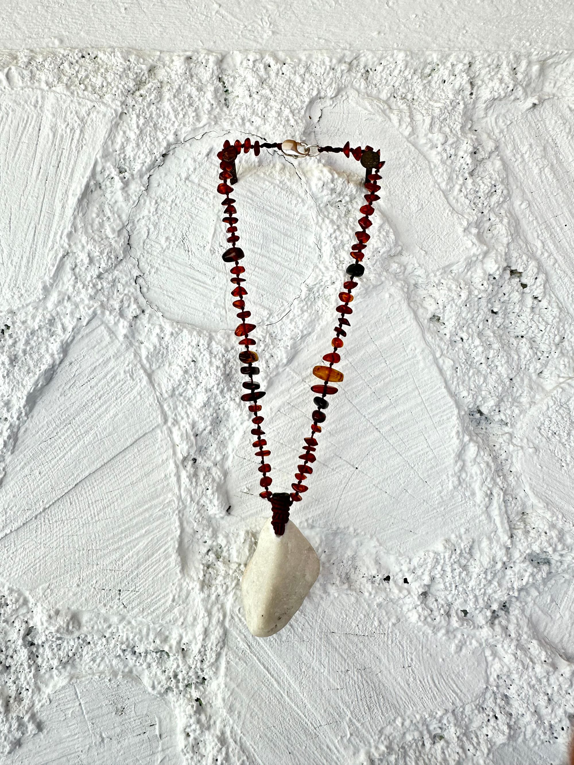 A necklace made of white river tumbled marble in a soft diamond shape is joined by beads of deep red orange Amber