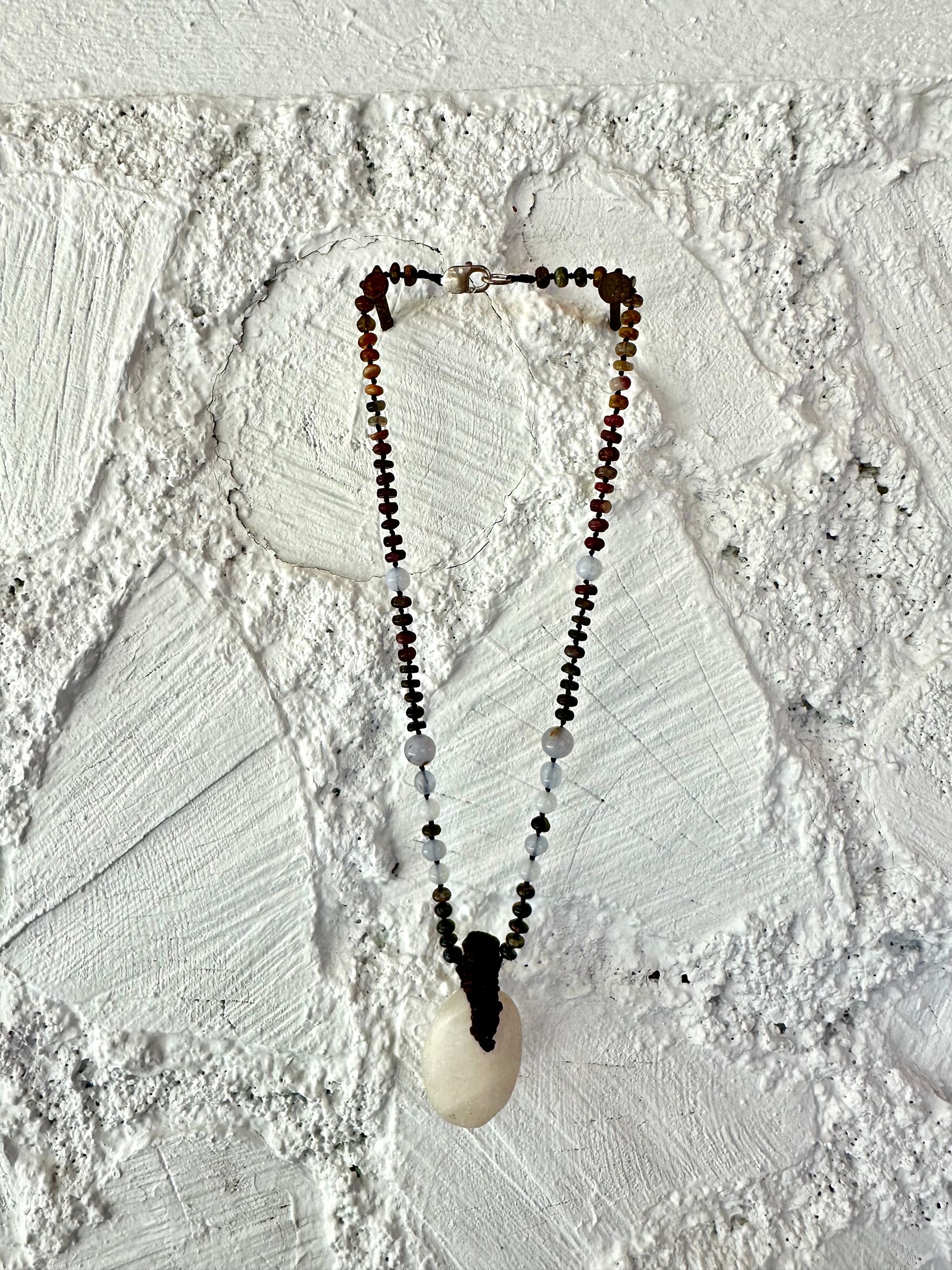 A necklace of an oval white ocean tumbled stone with a knot work vessel Growing from it is held by beads of luminous blue chalcedony and orange green, yellow and pink tourmaline