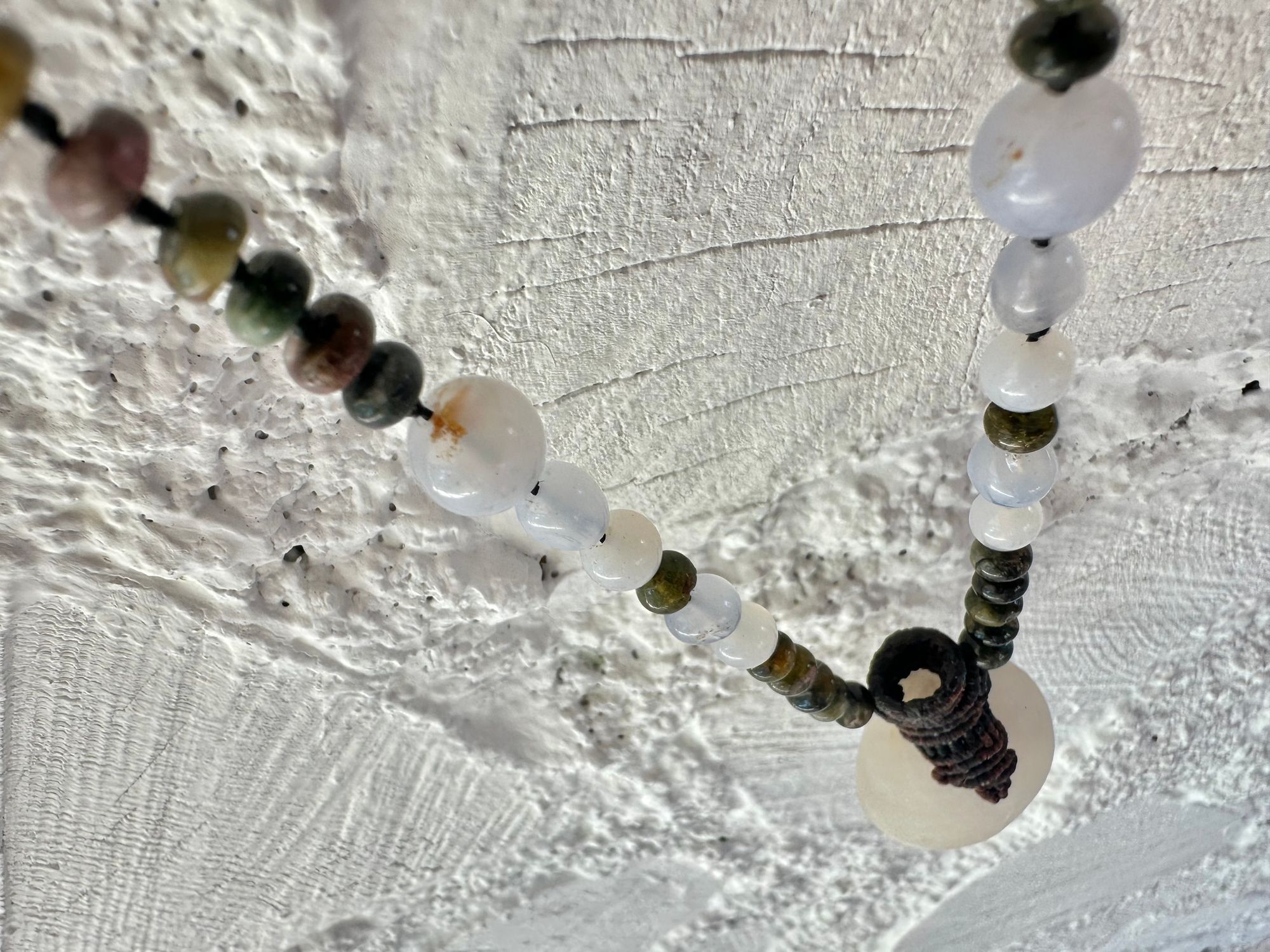 A necklace of an oval white ocean tumbled stone with a knot work vessel Growing from it is held by beads of luminous blue chalcedony and orange green, yellow and pink tourmaline