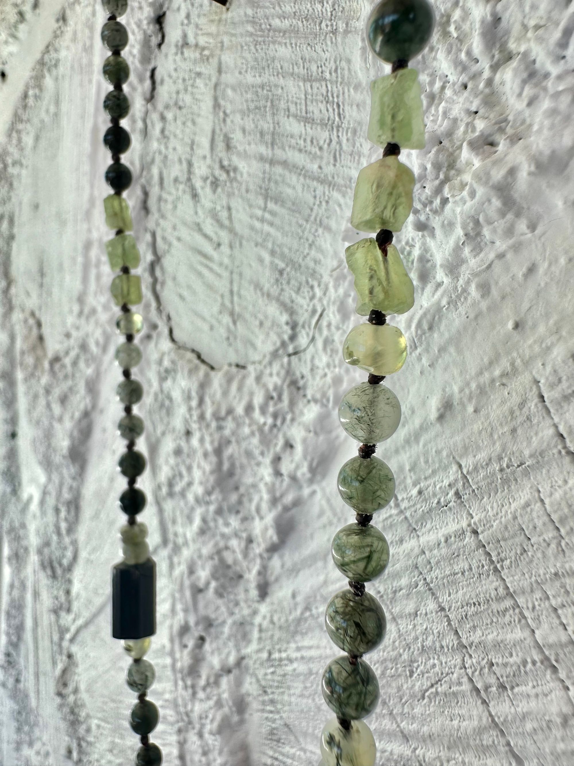 In necklace of raw emerald in its matrix with glittering pyrite is hanging from strands of delicate black work with green beads of rutile, quartz, peridot and black tourmaline