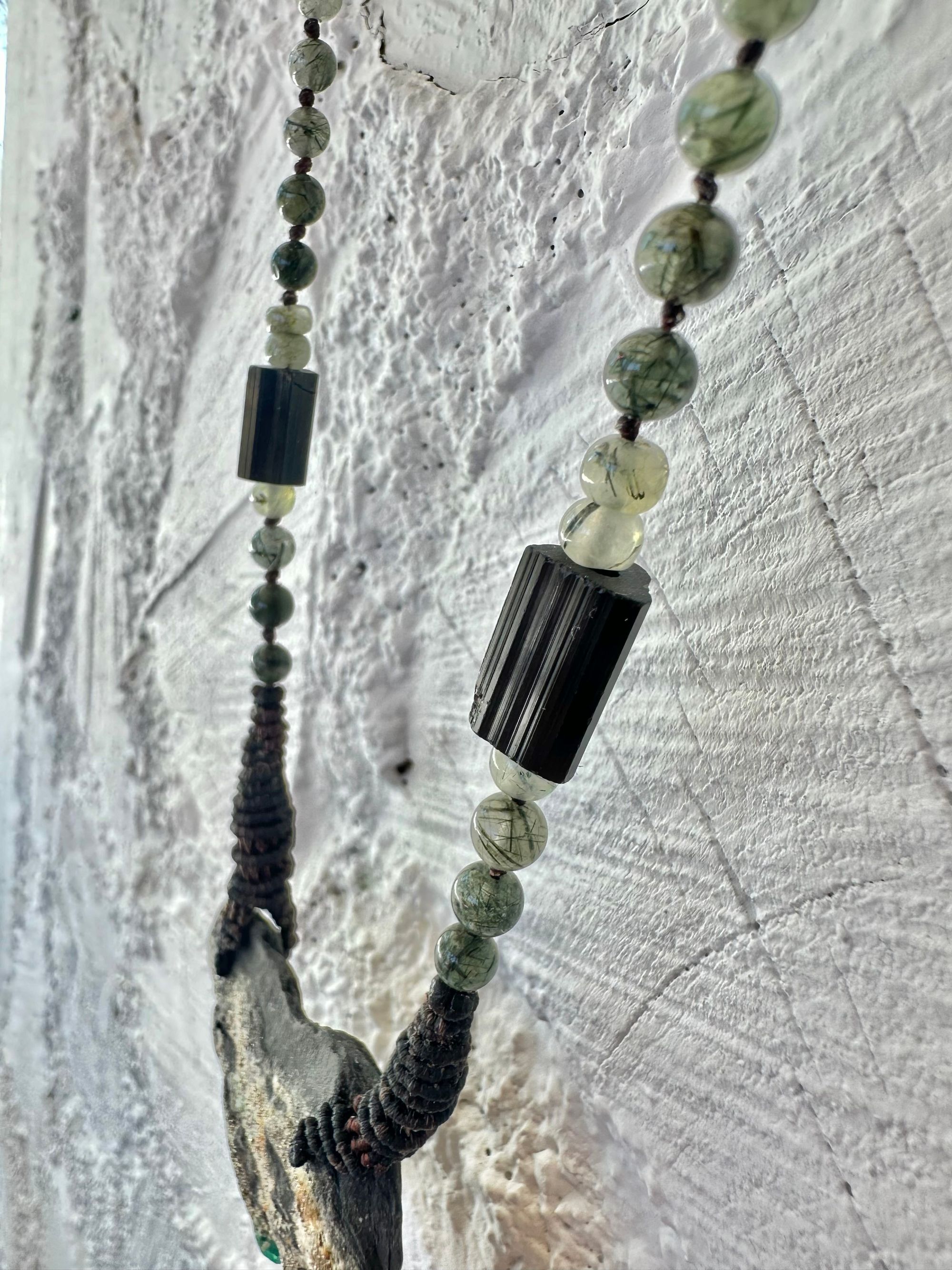 In necklace of raw emerald in its matrix with glittering pyrite is hanging from strands of delicate black work with green beads of rutile, quartz, peridot and black tourmaline