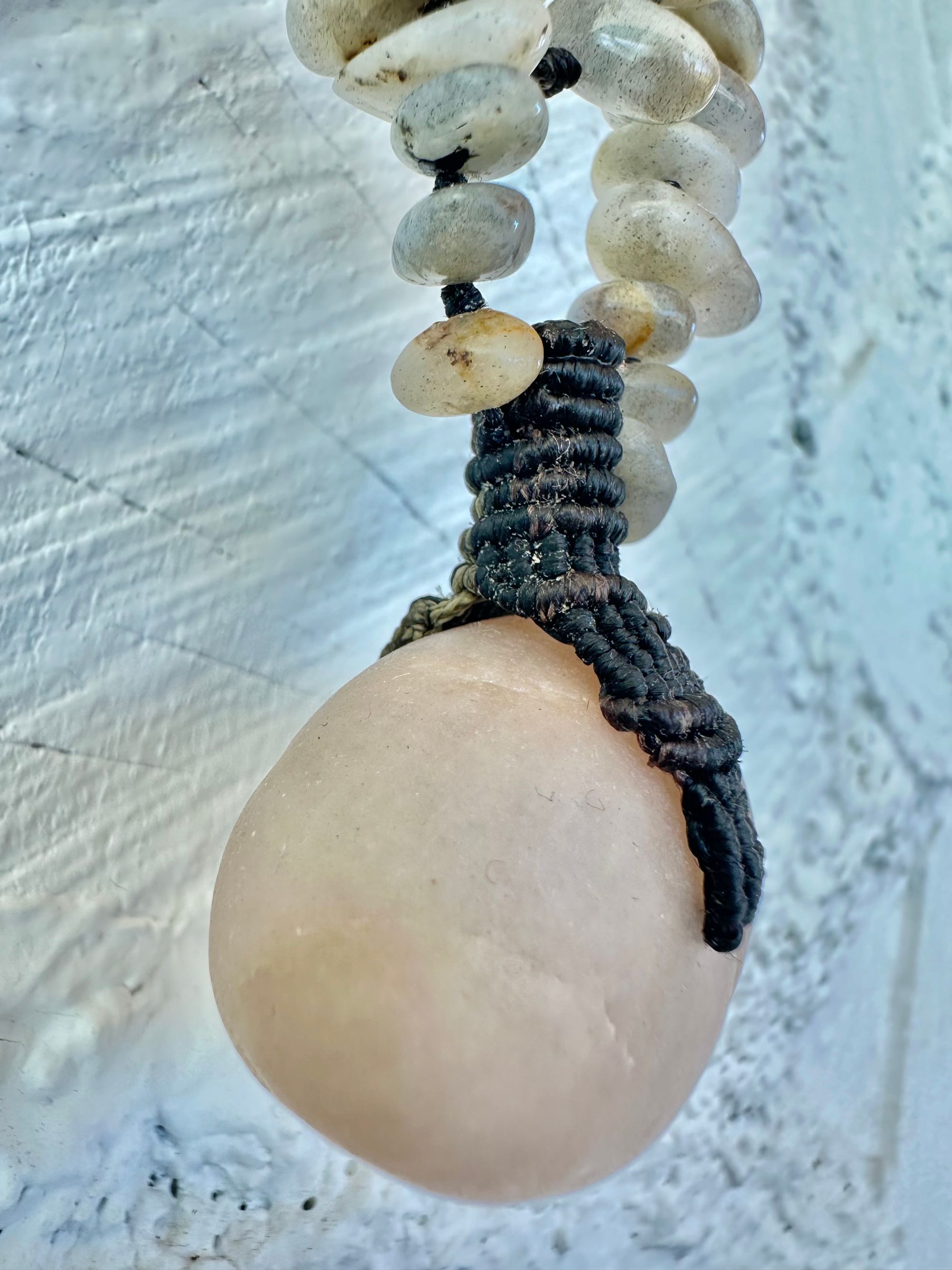 A detail of a necklace constructed from a White glowing ocean tumbled stone, From it was constructed a dark purple, knot work Basket, and from this Are irregularly shaped Beads of labradorite