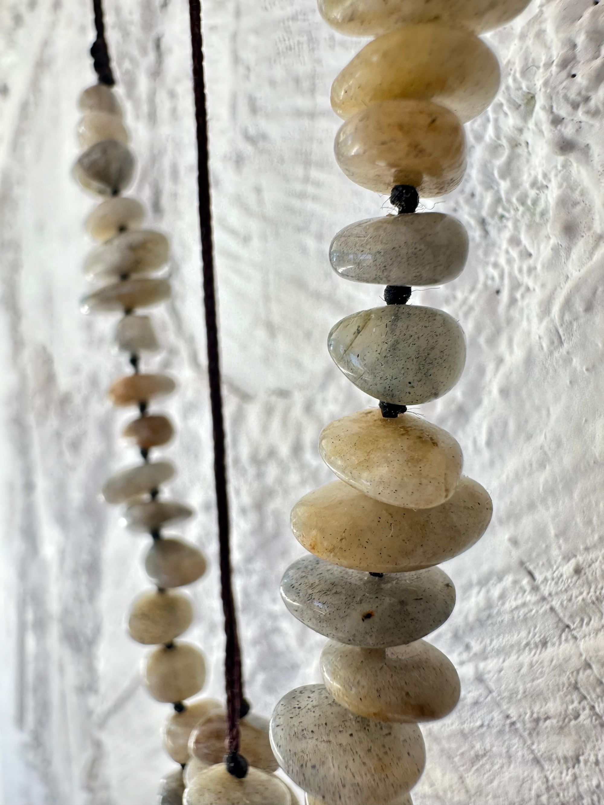 A detail of a necklace constructed from a White glowing ocean tumbled stone, From it was constructed a dark purple, knot work Basket, and from this Are irregularly shaped Beads of labradorite