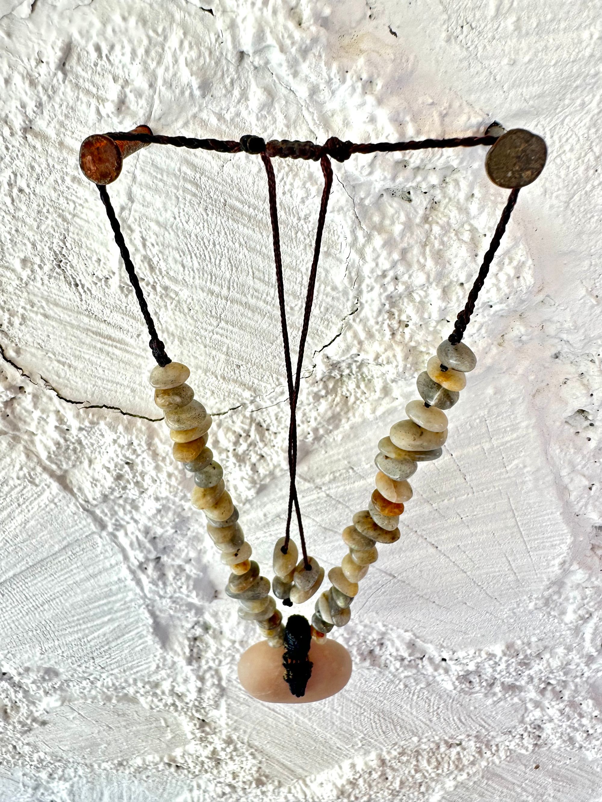 A detail of a necklace constructed from a White glowing ocean tumbled stone, From it was constructed a dark purple, knot work Basket, and from this Are irregularly shaped Beads of labradorite