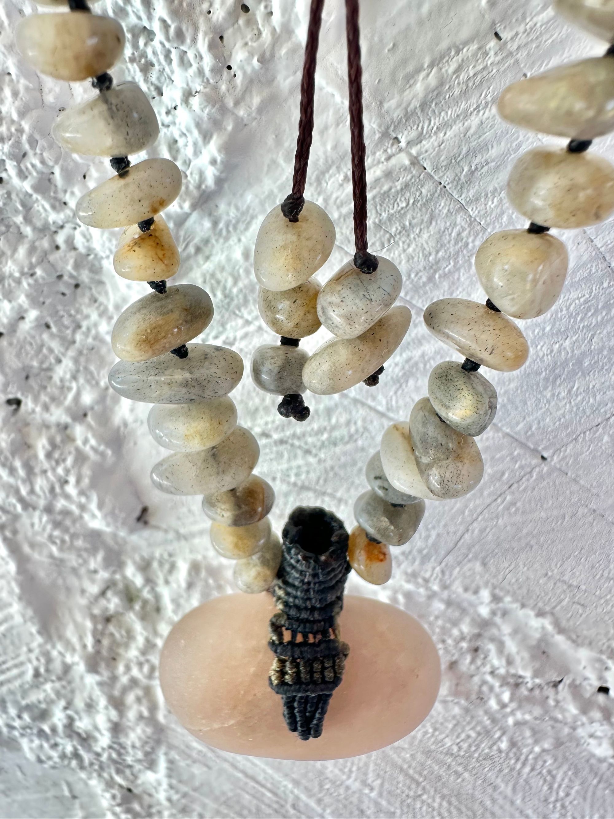 A detail of a necklace constructed from a White glowing ocean tumbled stone, From it was constructed a dark purple, knot work Basket, and from this Are irregularly shaped Beads of labradorite