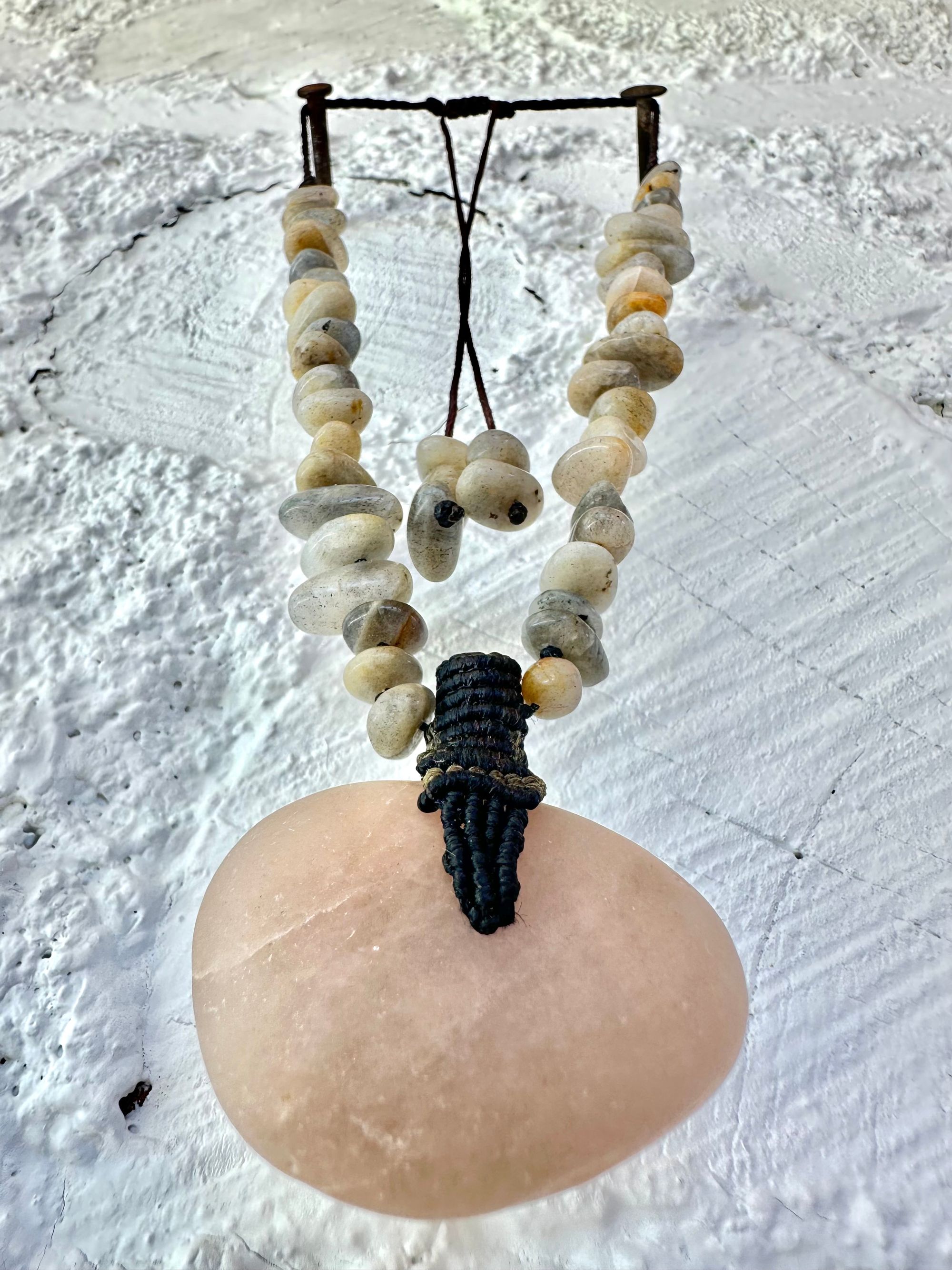 A detail of a necklace constructed from a White glowing ocean tumbled stone, From it was constructed a dark purple, knot work Basket, and from this Are irregularly shaped Beads of labradorite