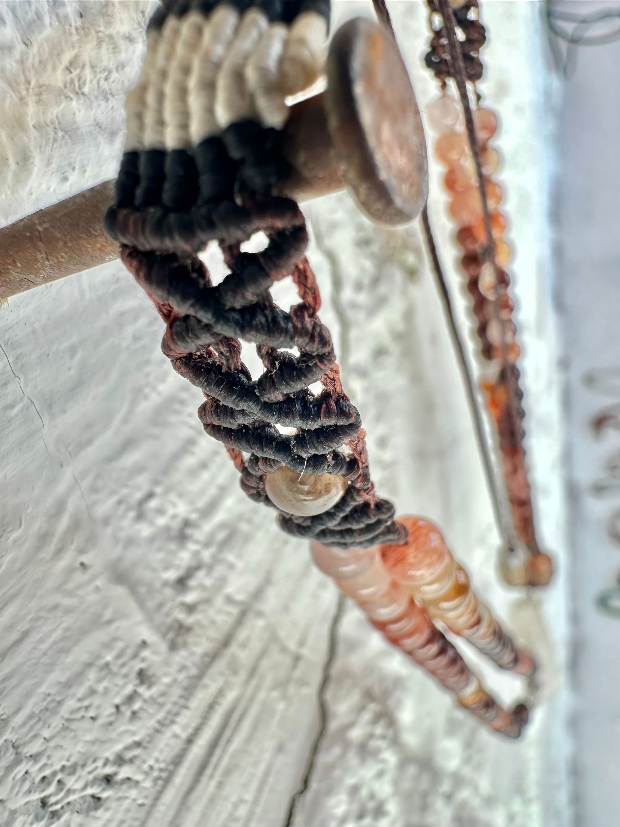 A necklace of clear quartz point with beads of deep hues of red ocre and soft pink hang against a white cordwood wall