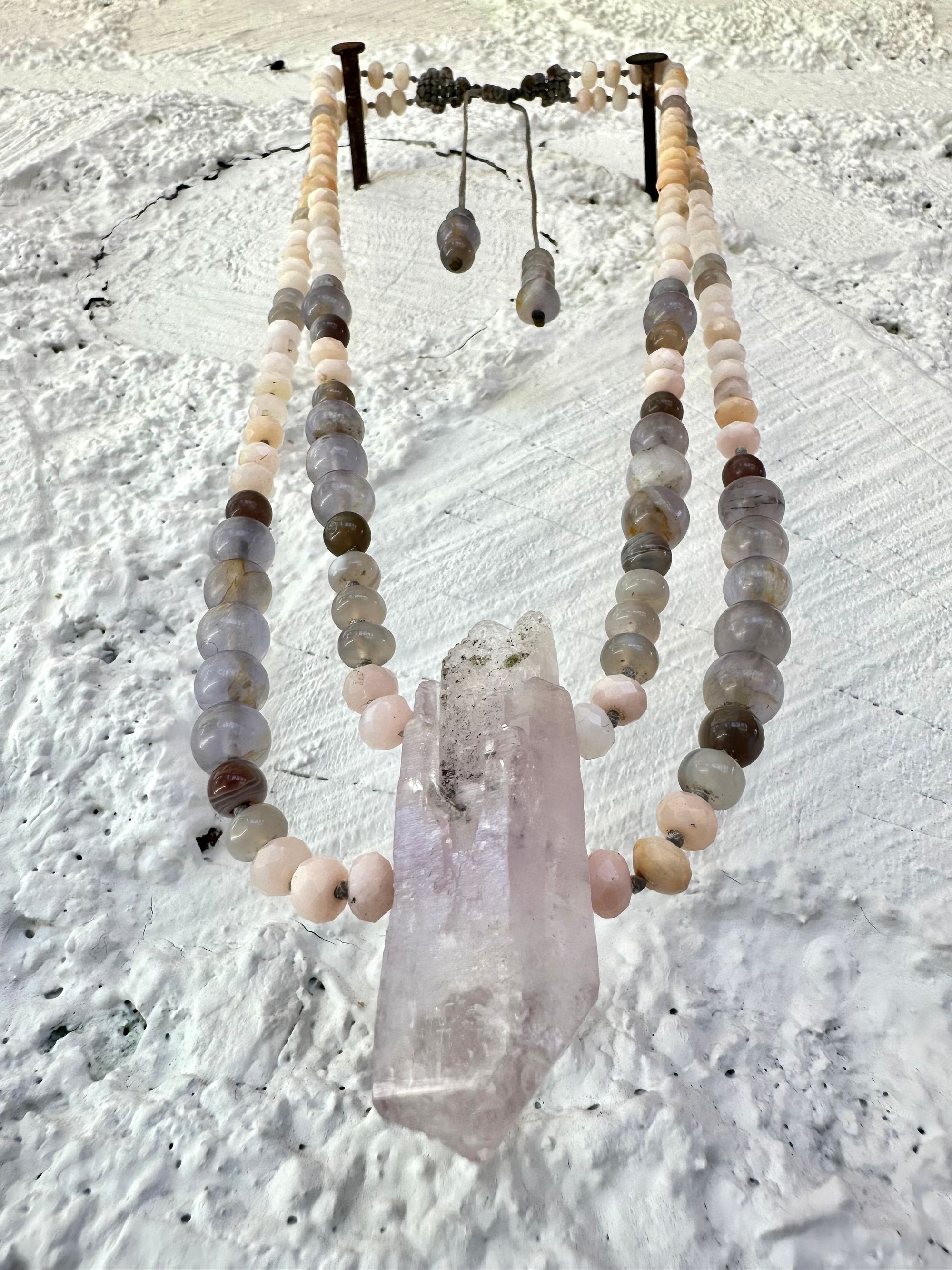 A necklace of soft but luminous, pink, purple and blue crystals hangs on a wall made of white painted cordwood