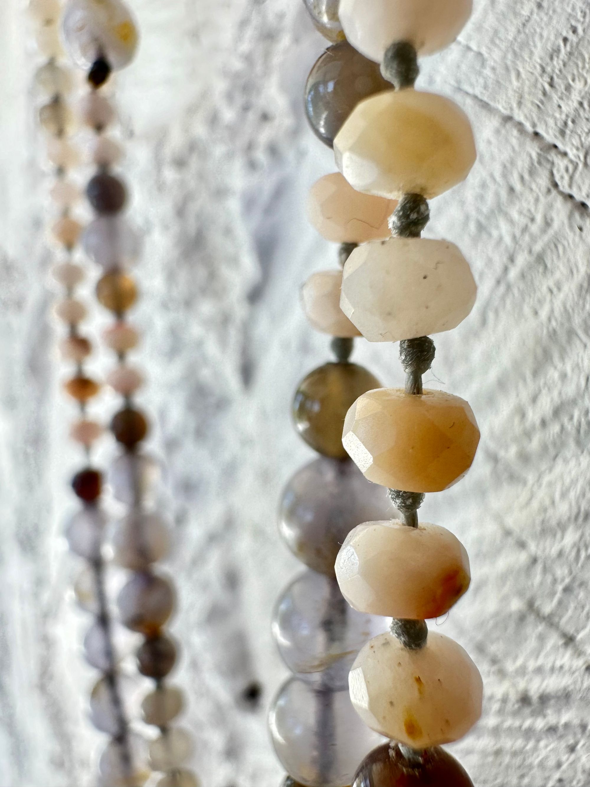 A necklace of soft but luminous, pink, purple and blue crystals hangs on a wall made of white painted cordwood