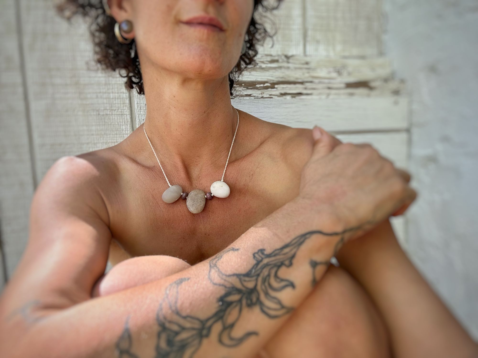 A woman wears a simple necklace of three white ocean tumbled stones on a white braided cord