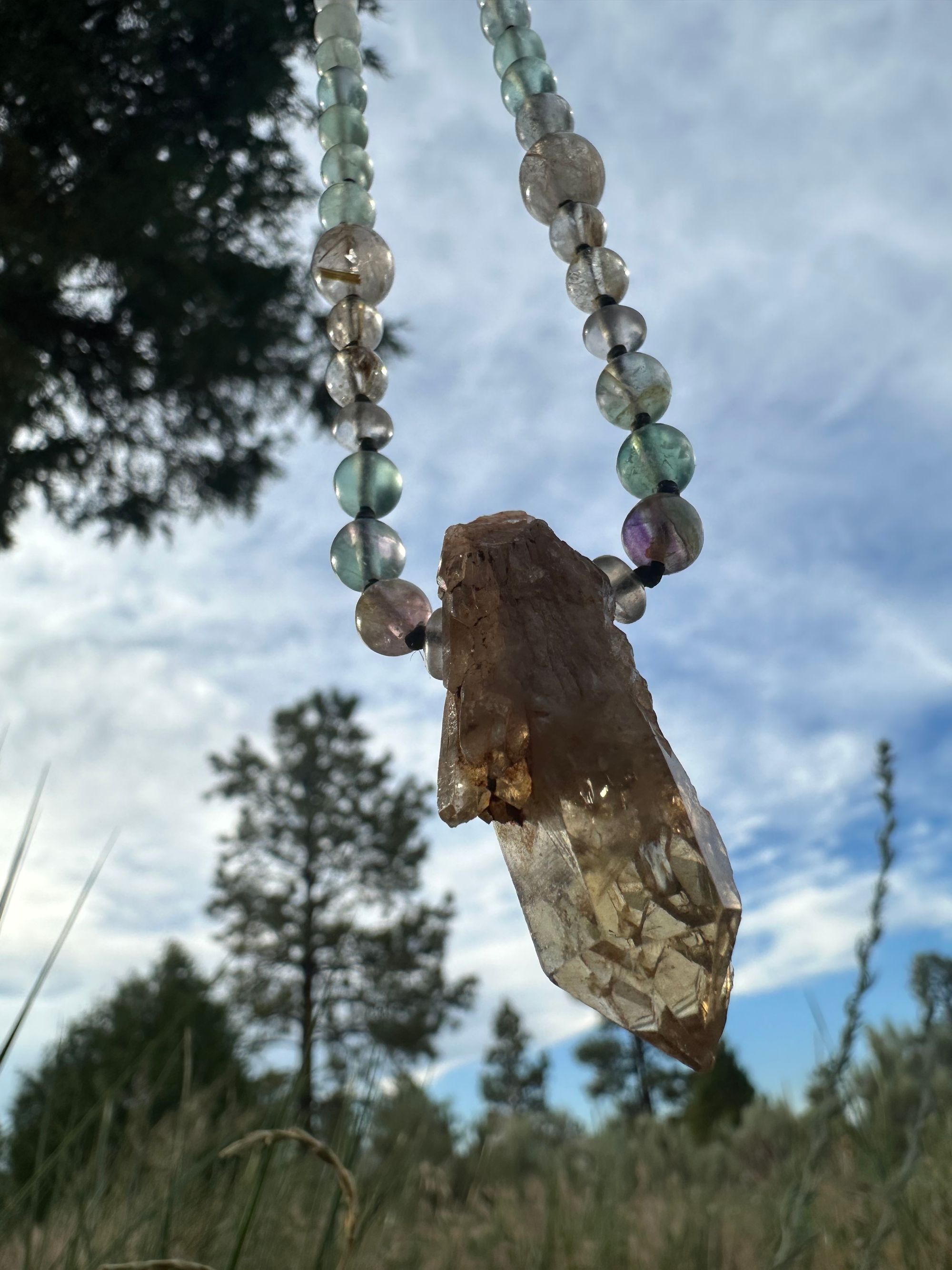 Yellow citrine and green fluorite necklace hangs against a blue sky in the forest