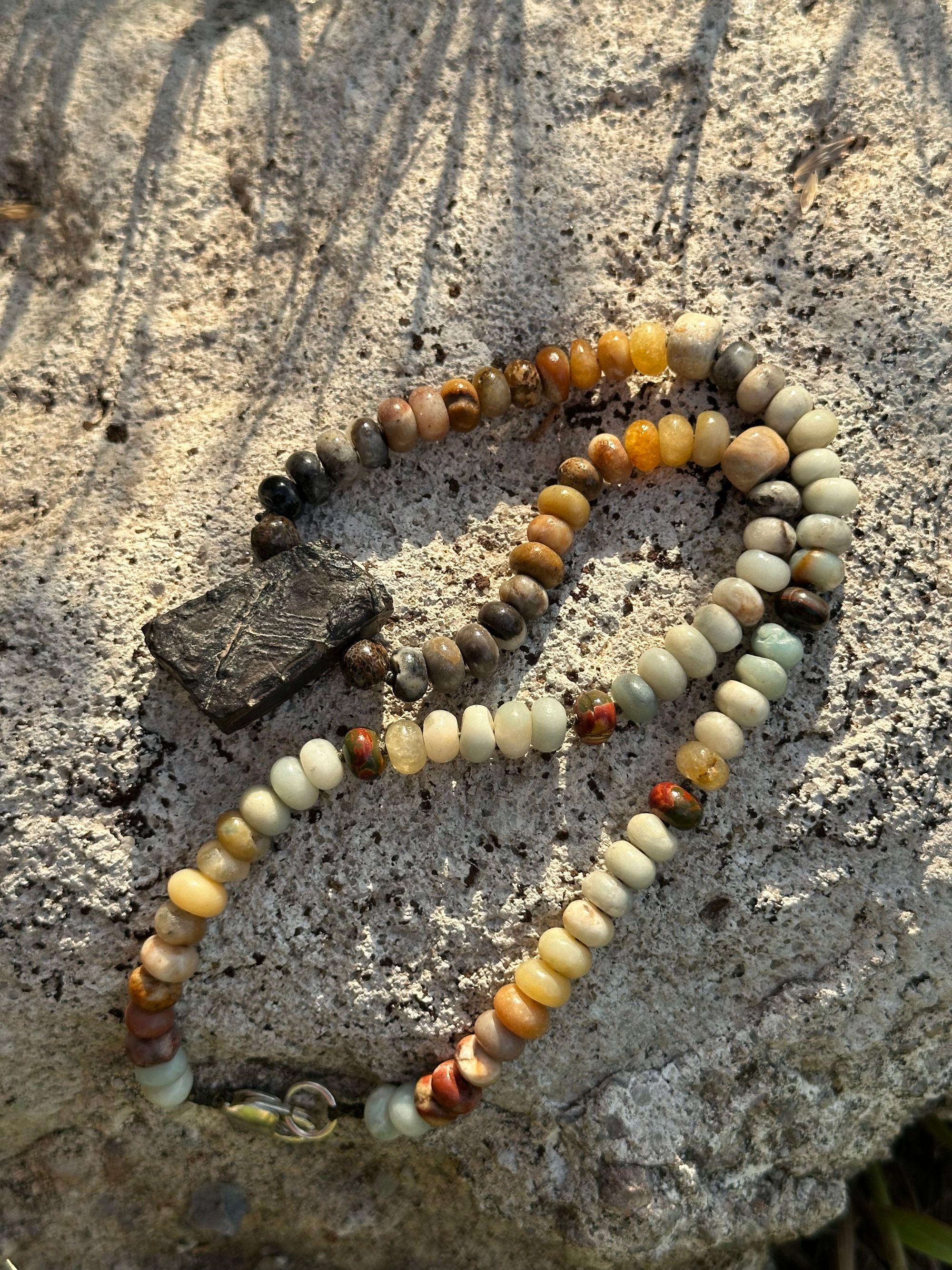 A necklace made of Gray, black and brown tsesit, A while, ancient stone is formed into an necklace with a rainbow of Jasper bees, petrified, dinosaur bone and fossilized coral