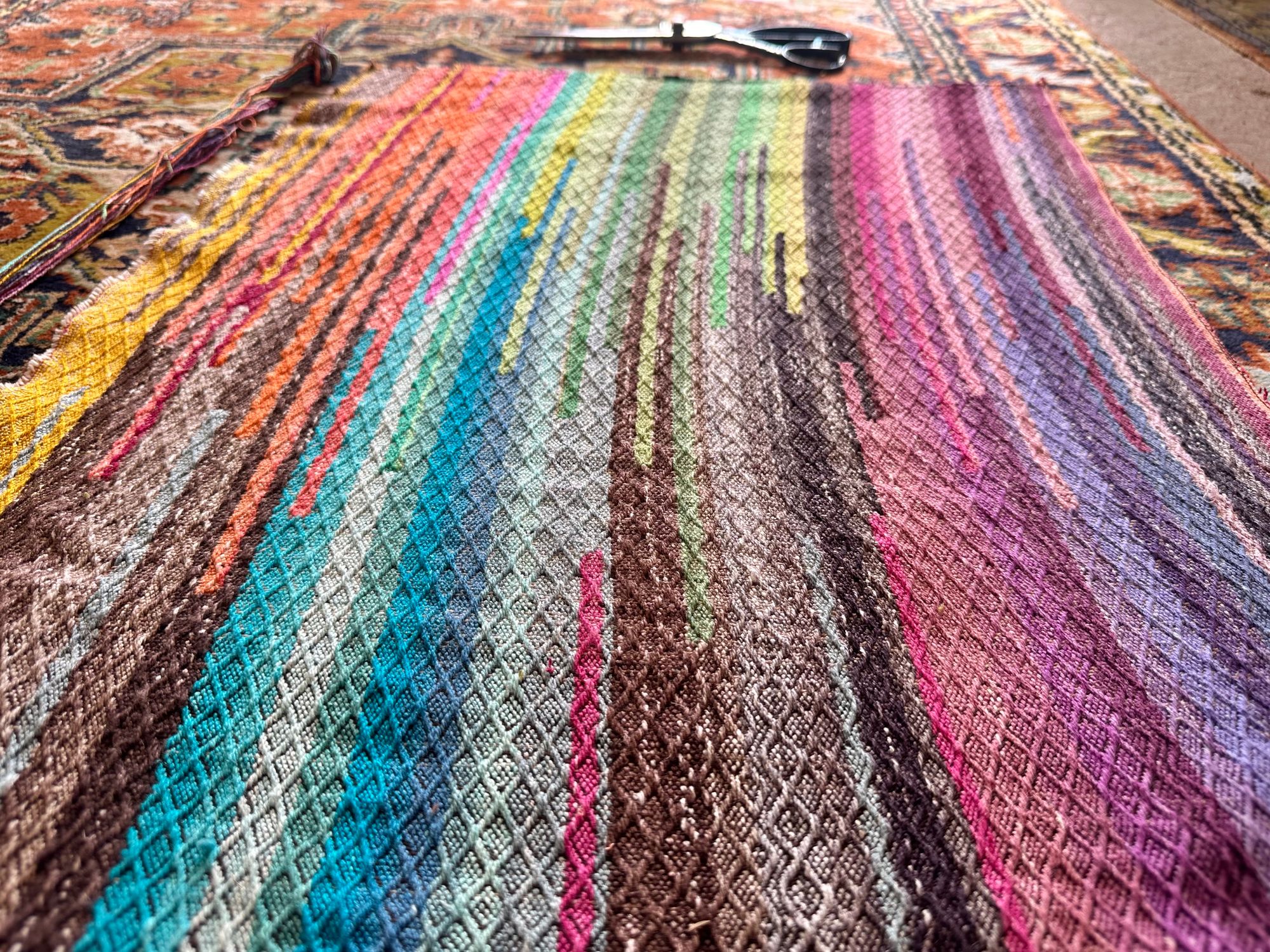 A small piece of hand woven fabric with a diamond texture, pattern, and bands of all the colors of the rainbow woven into it