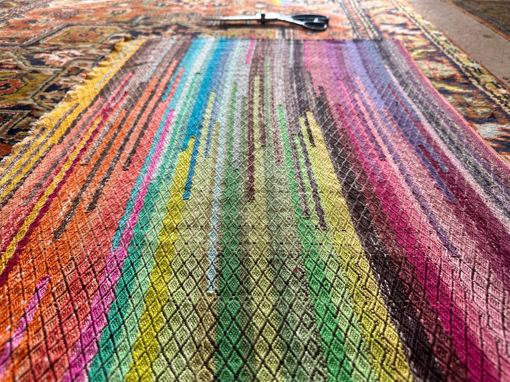 A small piece of hand woven fabric with a diamond texture, pattern, and bands of all the colors of the rainbow woven into it