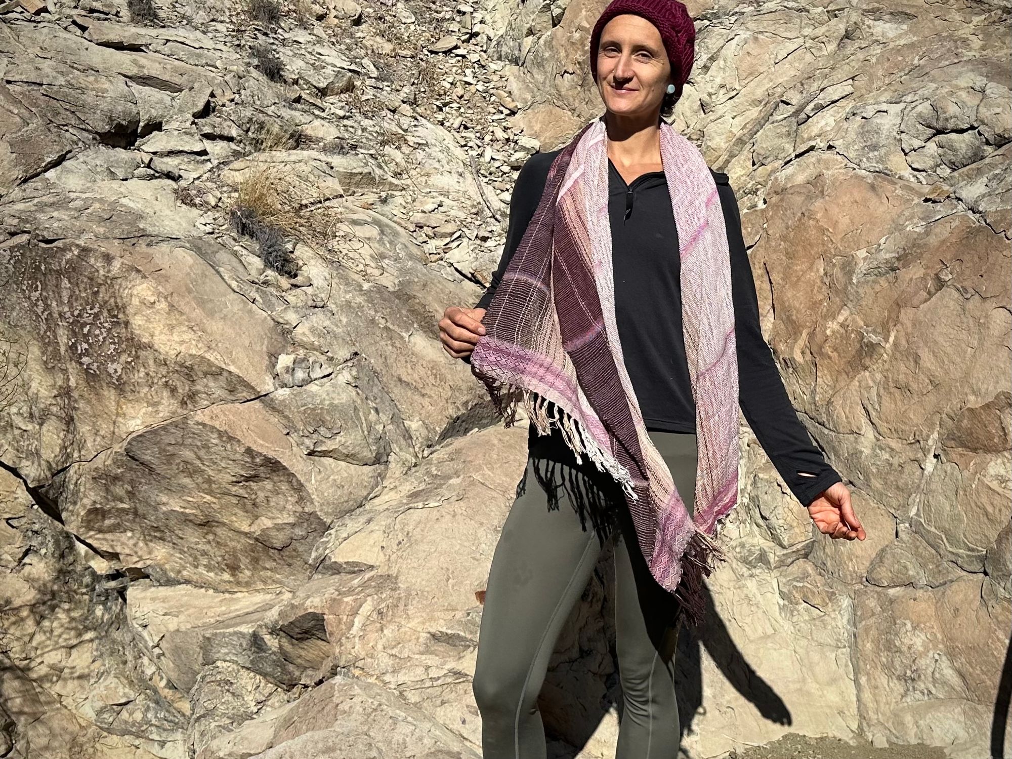 A woman stands in front of a cliff with a pink naturally dyed scarf