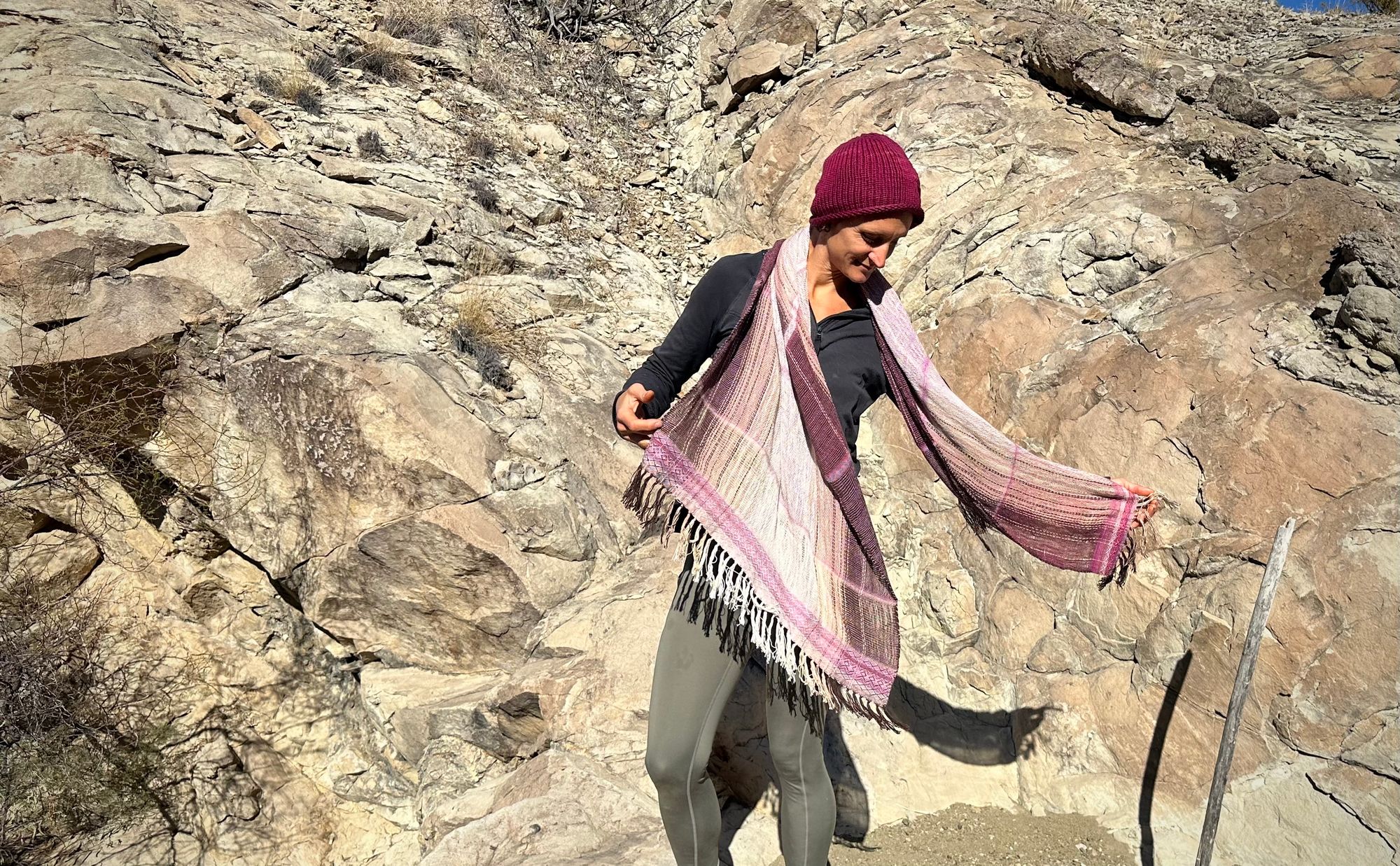 A woman stands in front of a cliff with a pink naturally dyed scarf