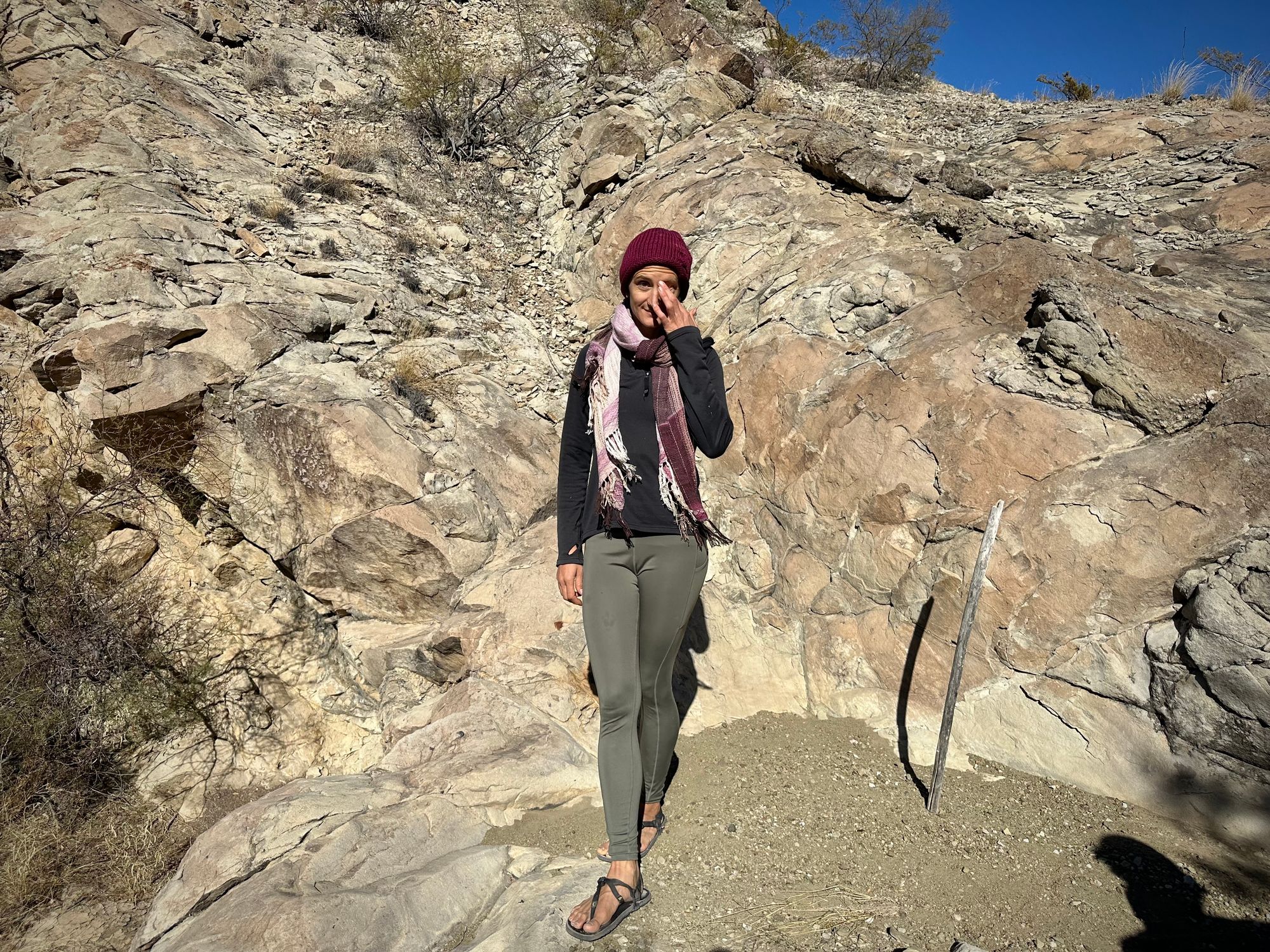 A woman stands in front of a cliff with a pink naturally dyed scarf