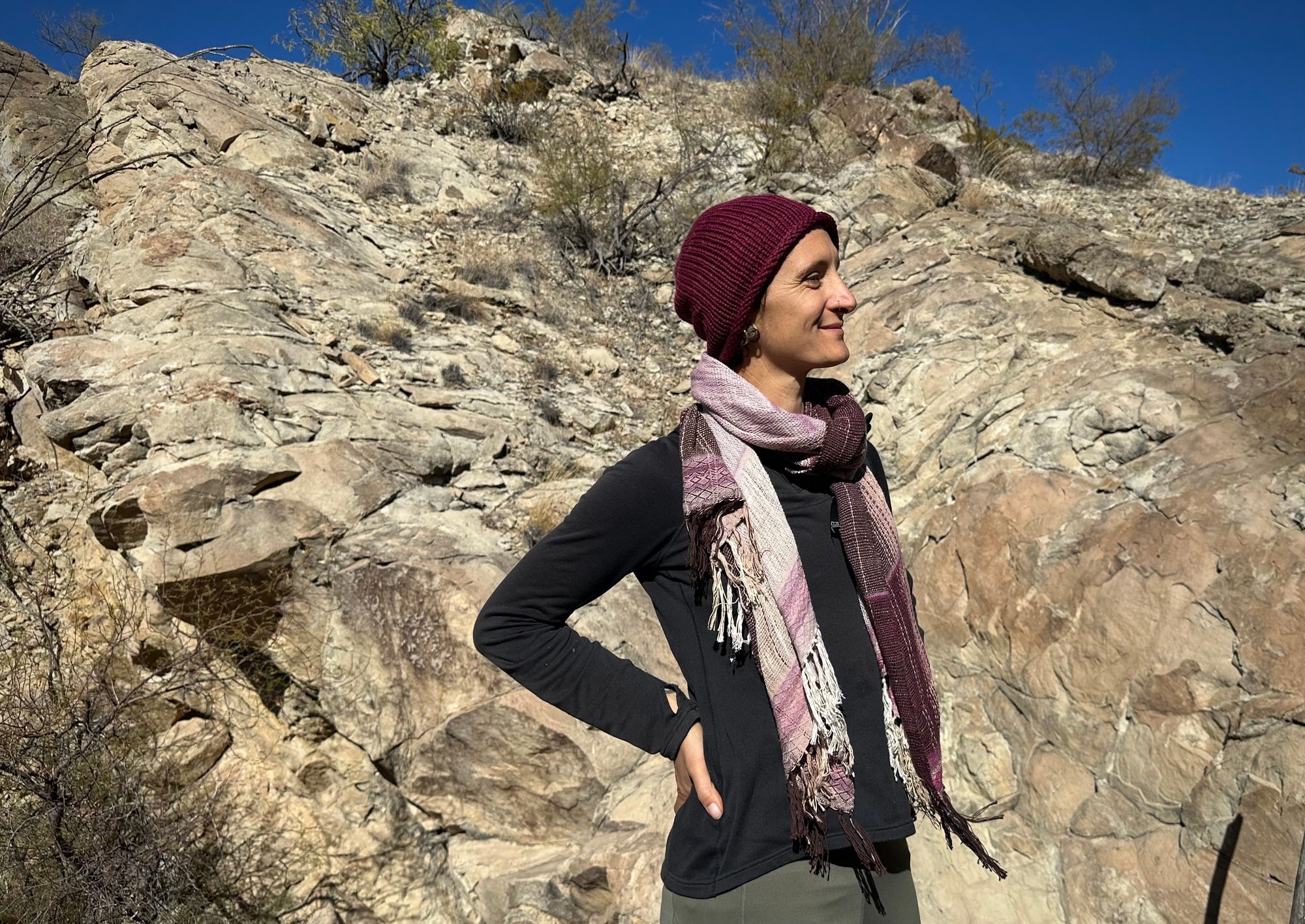 A woman stands in front of a cliff with a pink naturally dyed scarf