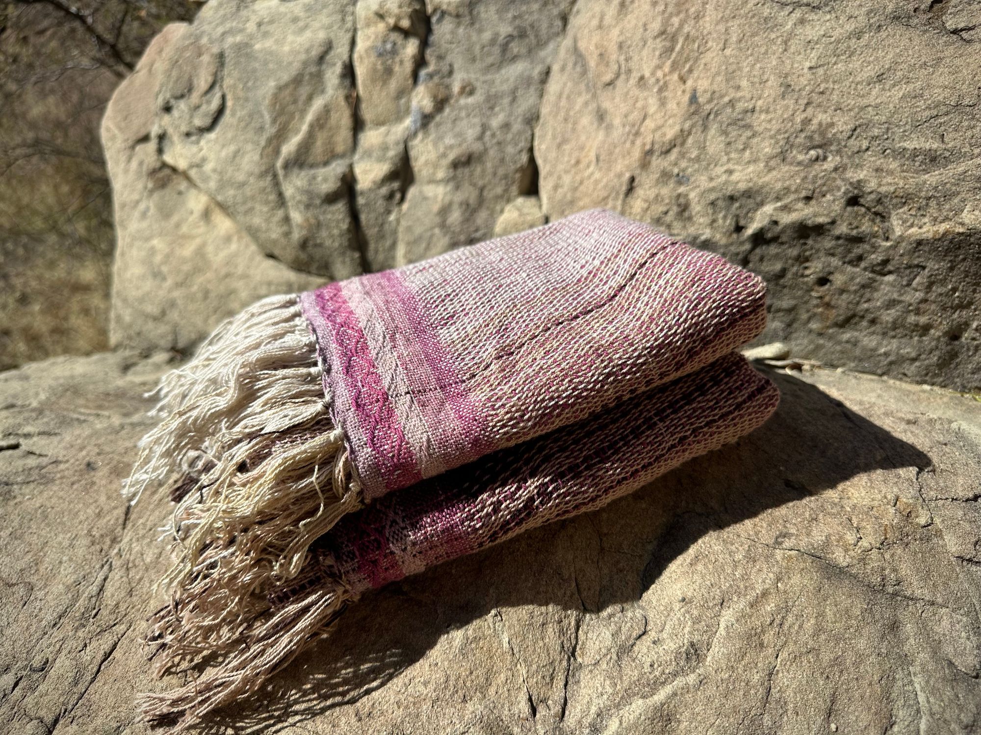 A naturally dyed scarf in pinks and lavender lays folded on a gray cliff