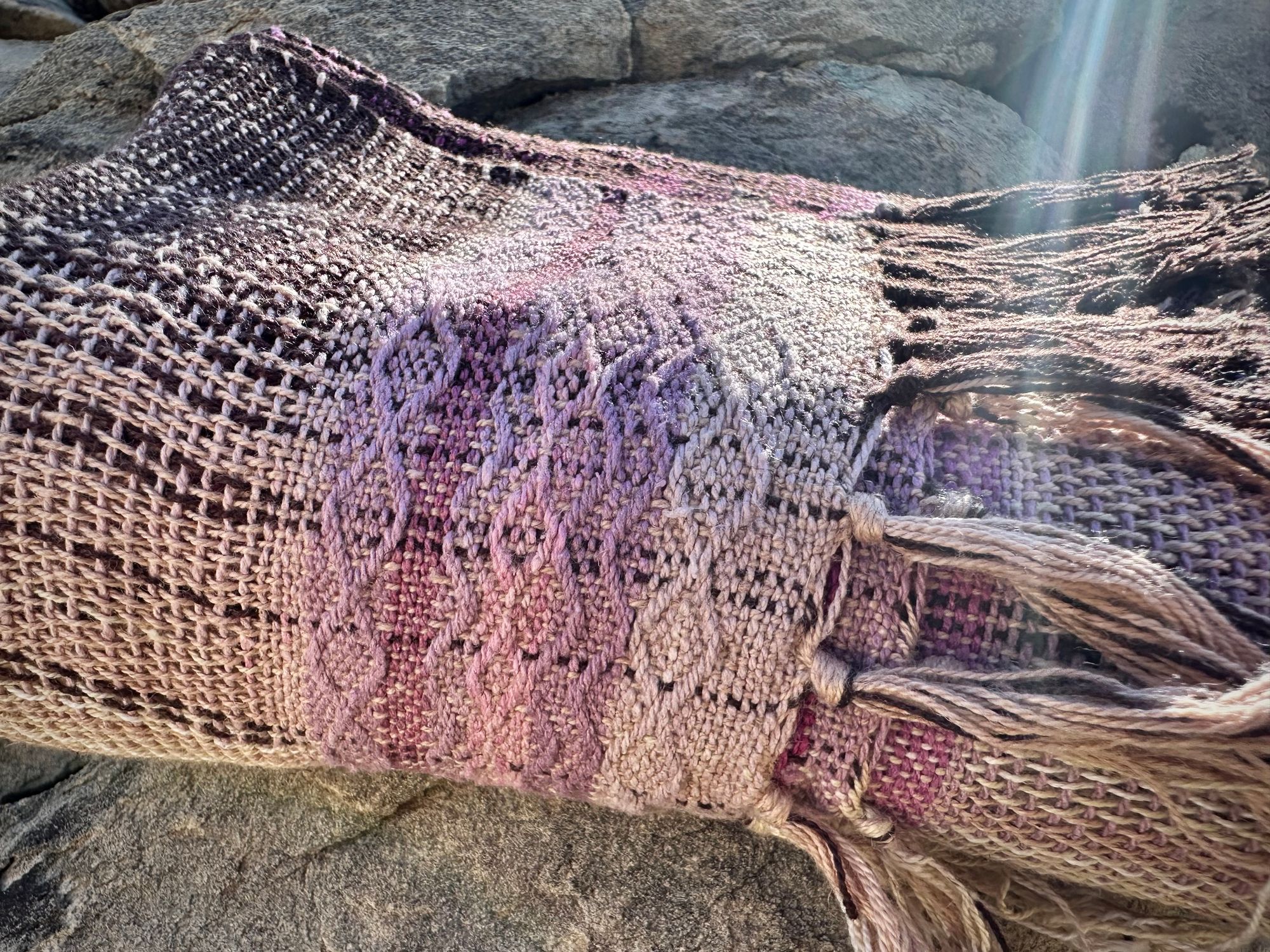 A naturally dyed scarf in pinks and lavender lays folded on a gray cliff