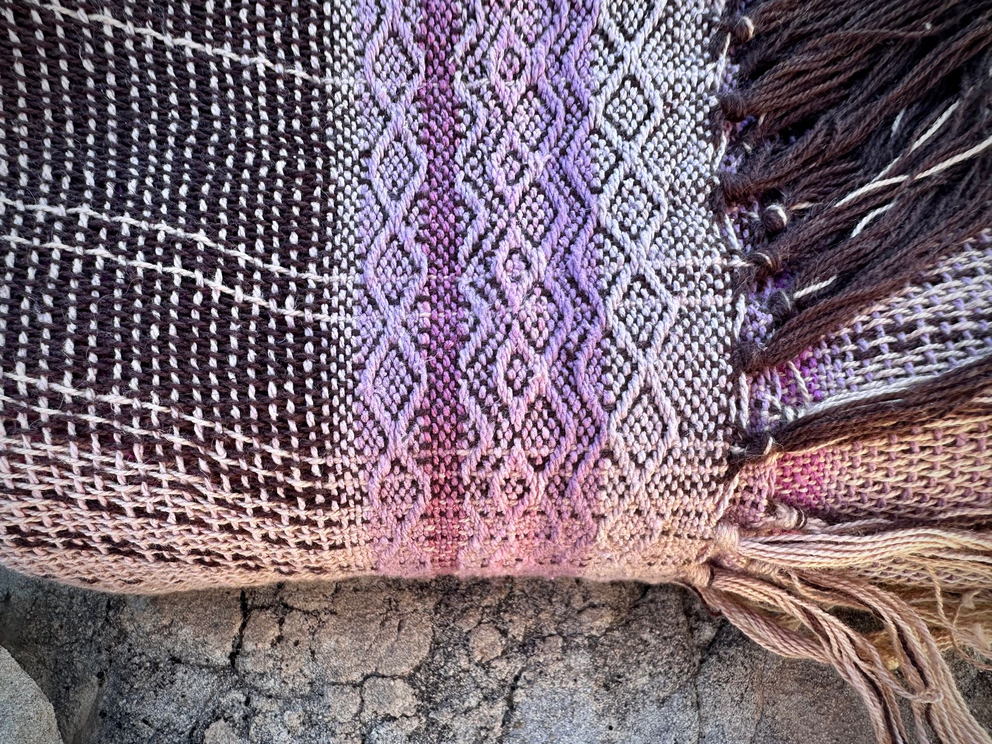 A naturally dyed scarf in pinks and lavender lays folded on a gray cliff