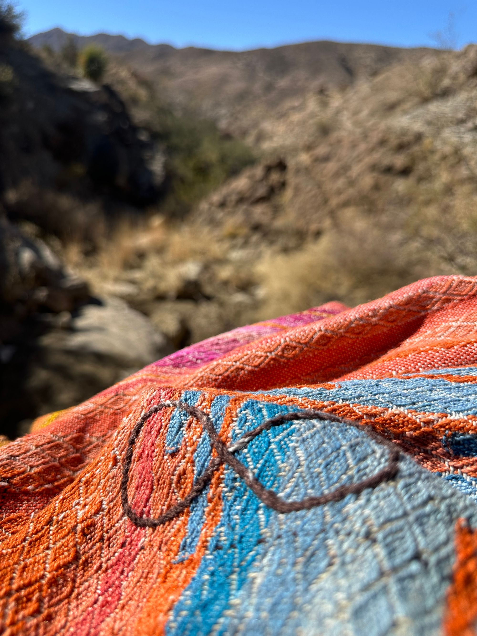 a detail of a handwoven infinity sign on a shawl that is orange, red, pink, and blue