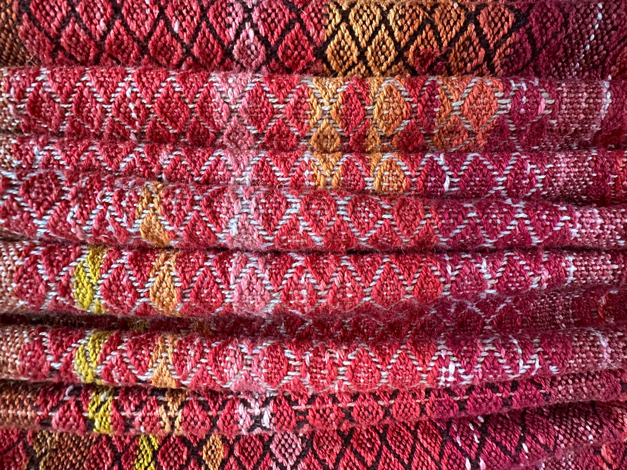 a detail of handwoven diamond pattern fabric in shades of red