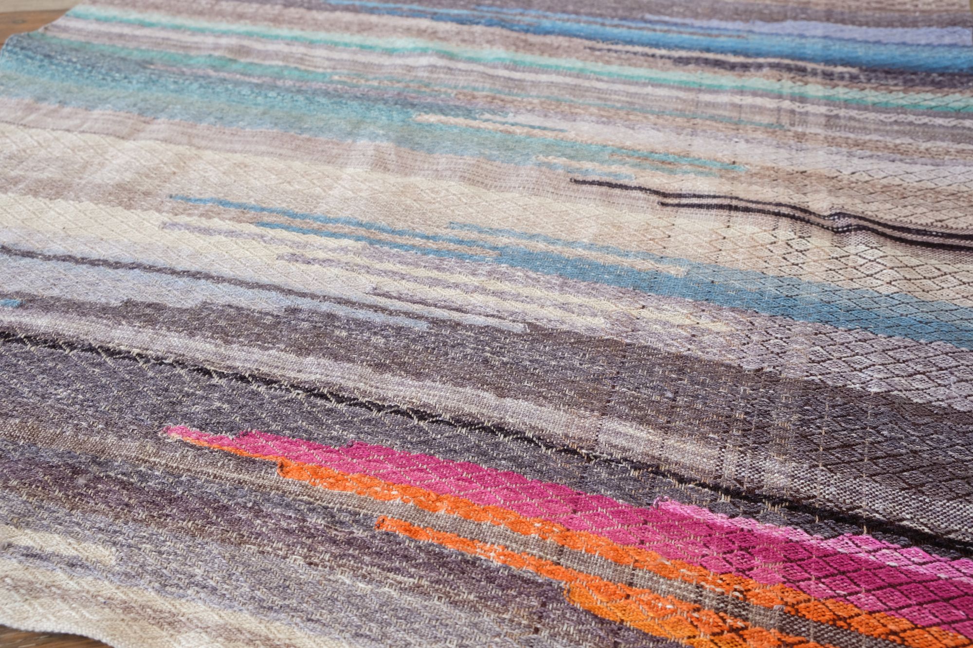 A detail image of a handwoven piece of fabric with a texture diamond pattern in shades of gray and blue With a splash of pink and marmalade orange