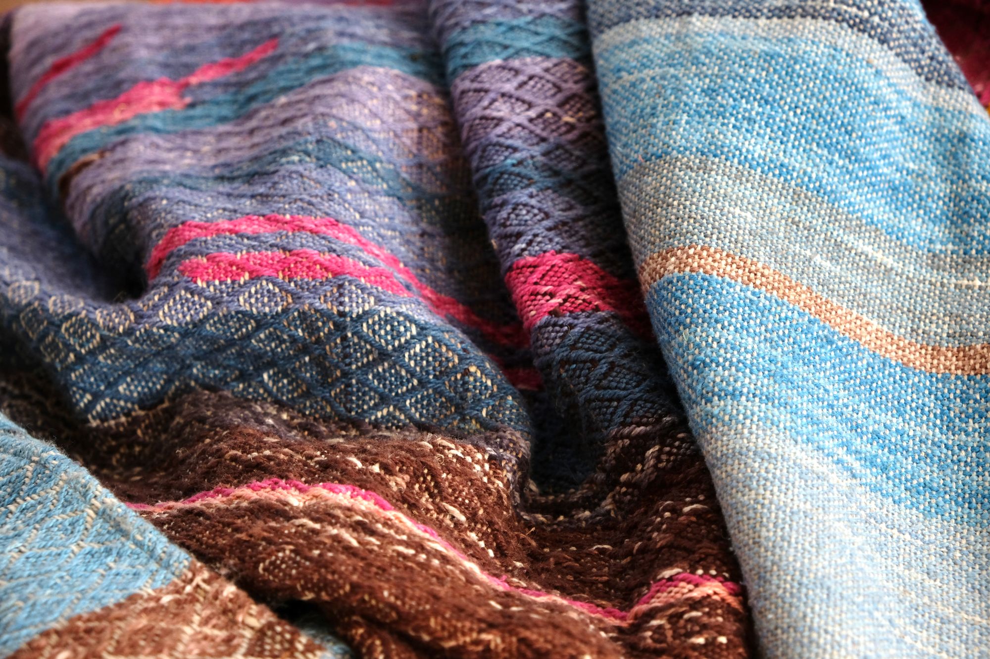 A length of handwoven fabric in earth hues as well as rainbow and sunrise colors lays on a wooden floor