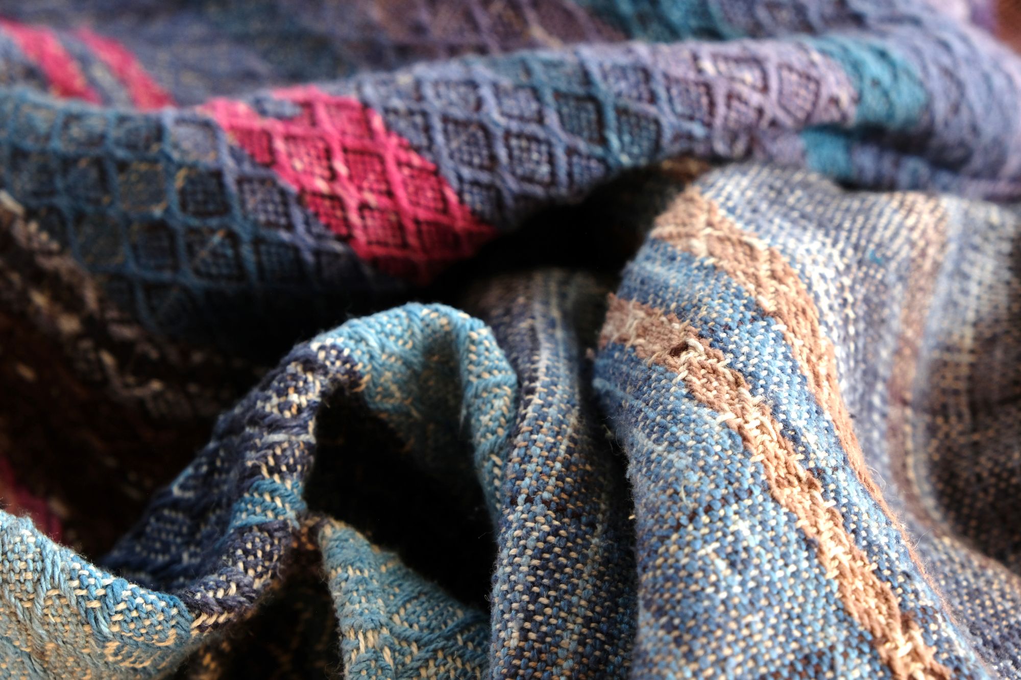 A length of handwoven fabric in earth hues as well as rainbow and sunrise colors lays on a wooden floor