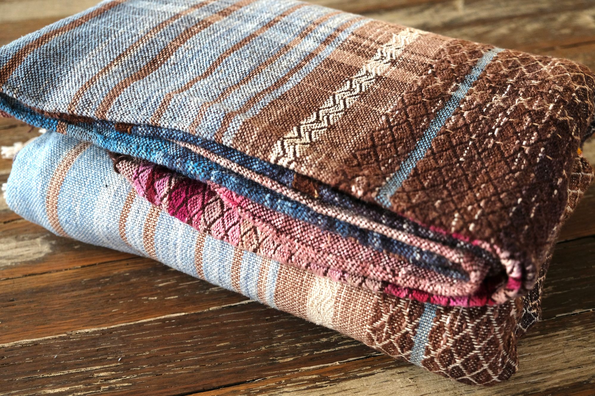 A length of handwoven fabric in earth hues as well as rainbow and sunrise colors lays folded on a wooden floor