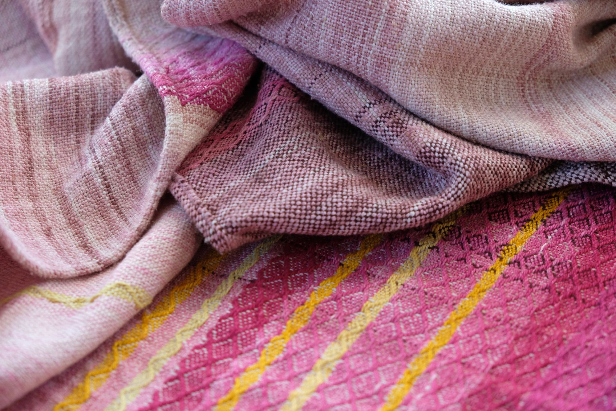 A length of handwoven fabric in earth hues as well as rainbow and sunrise colors lays on a wooden floor