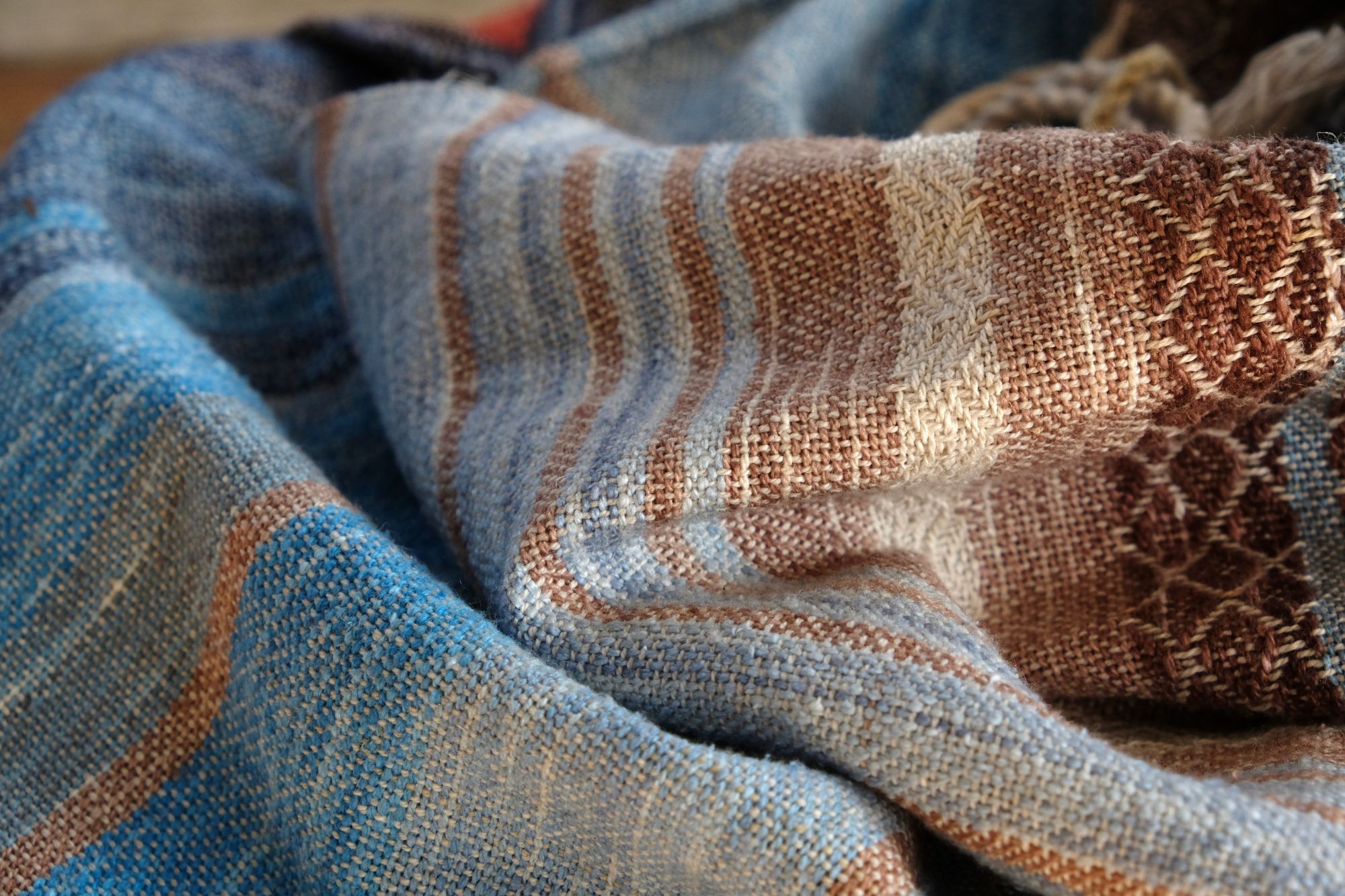 A length of handwoven fabric in earth hues as well as rainbow and sunrise colors lays on a wooden floor