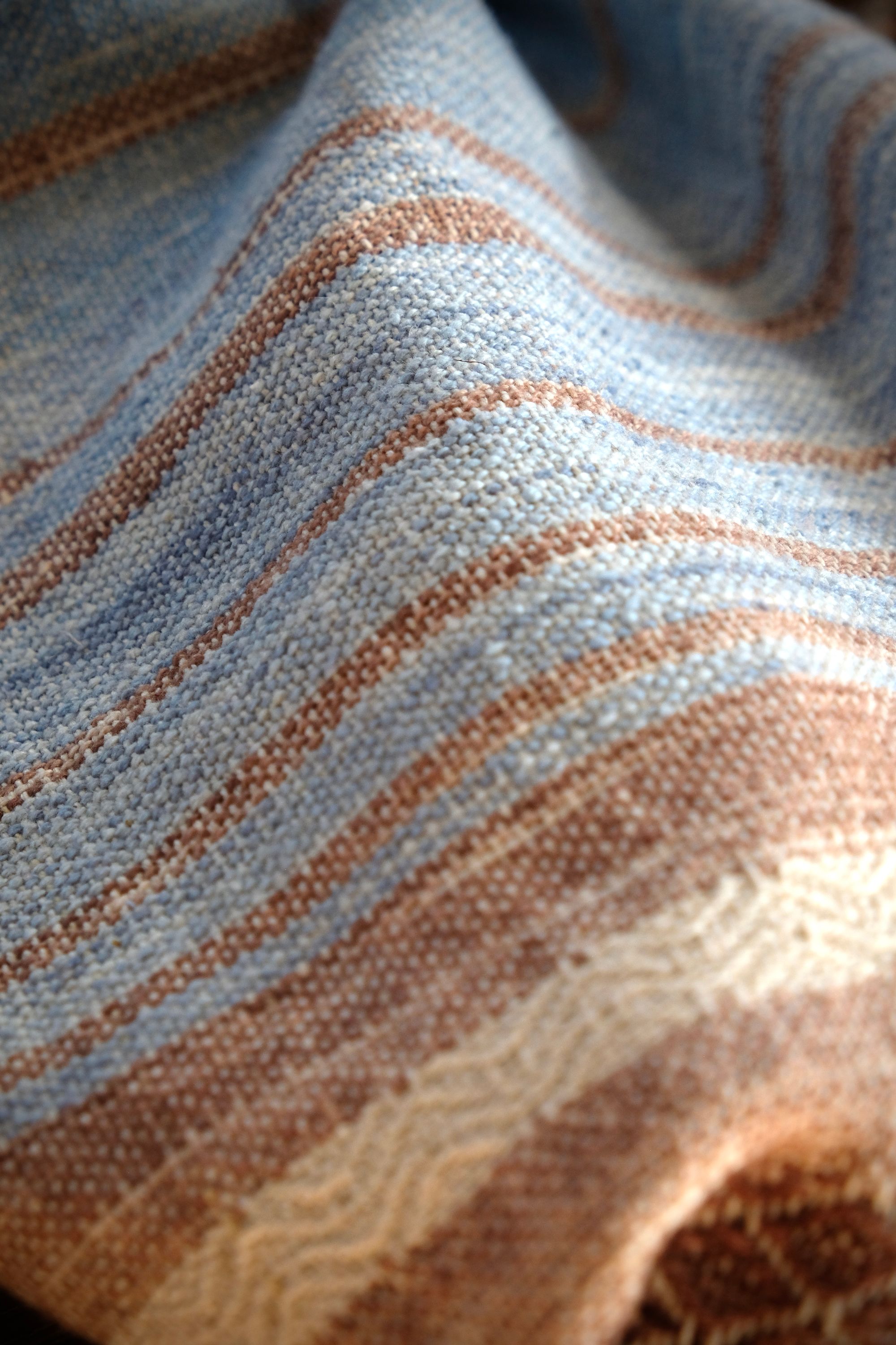 A length of handwoven fabric in earth hues as well as rainbow and sunrise colors lays on a wooden floor