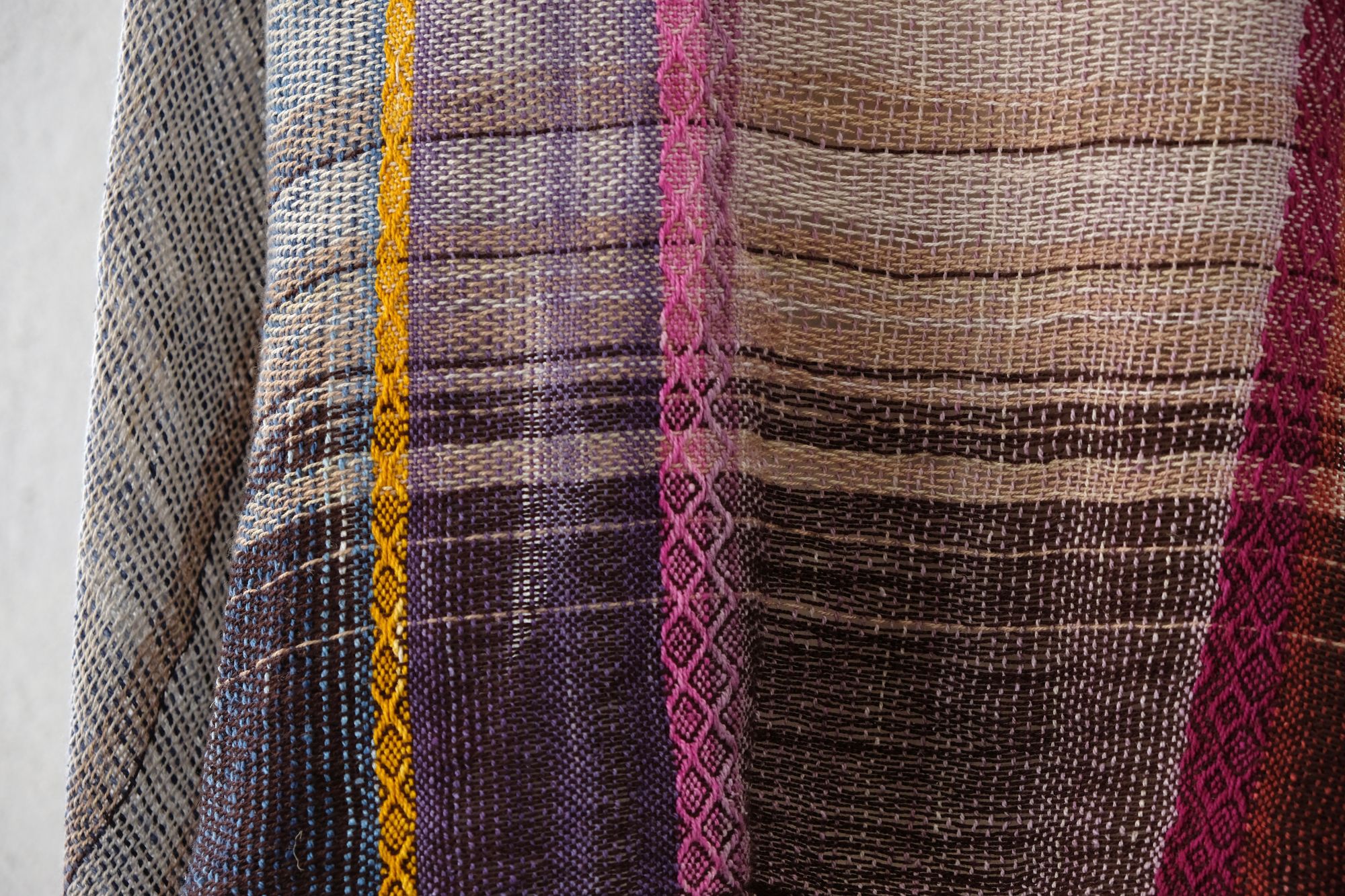 A white painted mannequin stands on a wooden speaker wearing an etherial handwoven scarf with a mixture of loose weave and rainbow shades, in rainbow hues